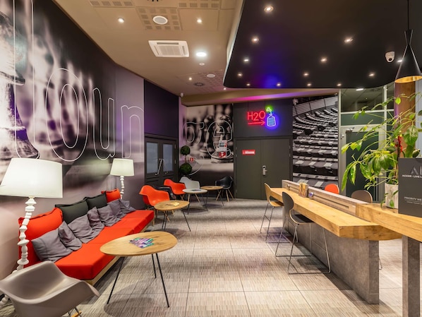 A modern lounge area with seating, a reception desk, and a neon sign indicating a water dispenser.