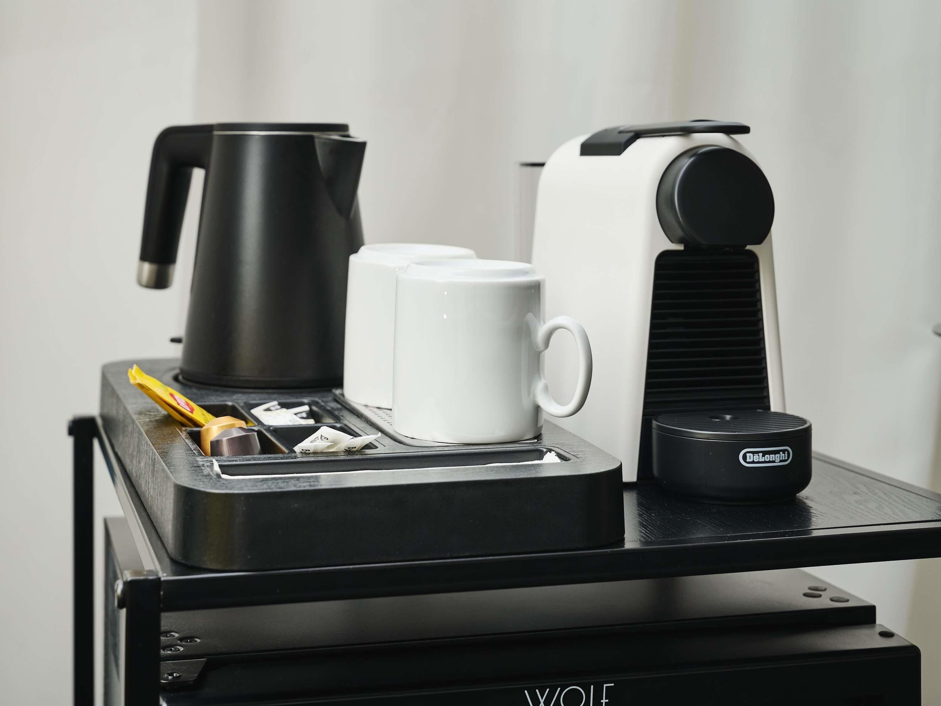 Une machine à café au design noir et blanc, une cafetière, deux tasses blanches et un moulin à café, le tout posé sur une surface noire.