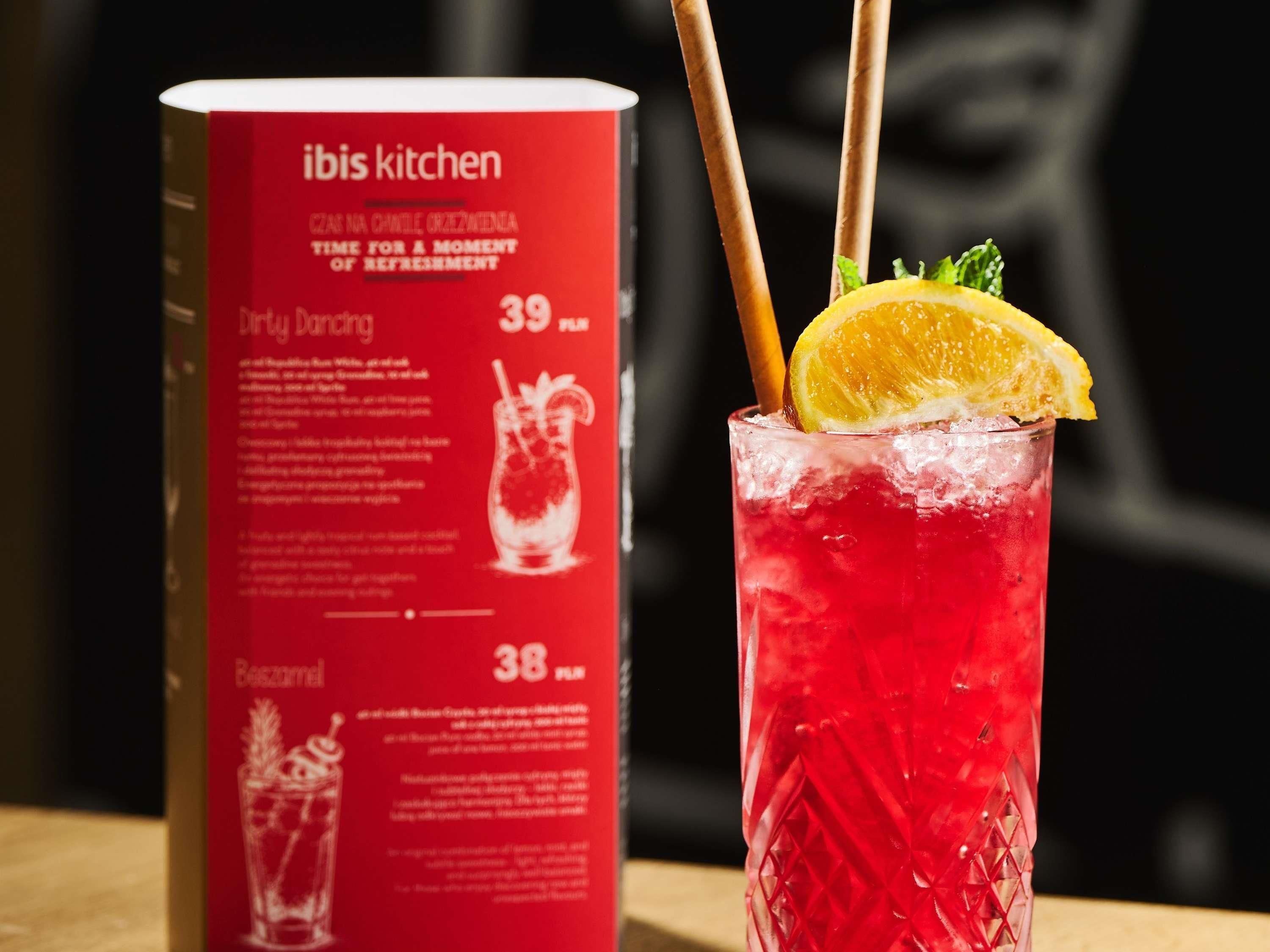 A menu with drink options and a glass of red beverage with a lemon slice and straw.