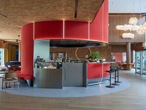 Un espace bar moderne doté d’un comptoir incurvé, de sièges et d’un grand luminaire suspendu.
