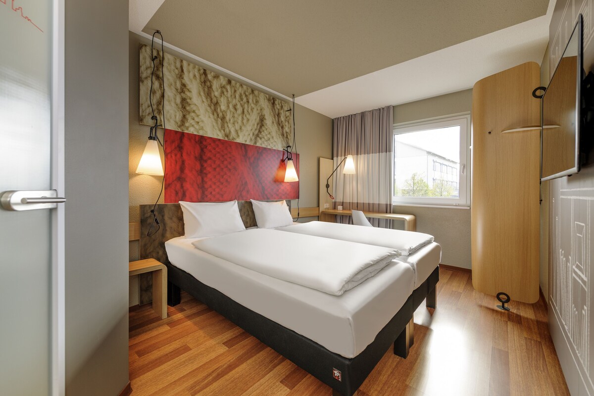 Une chambre d’hôtel avec un lit double, des tables de chevet, un bureau, une chaise, une télévision et une armoire.