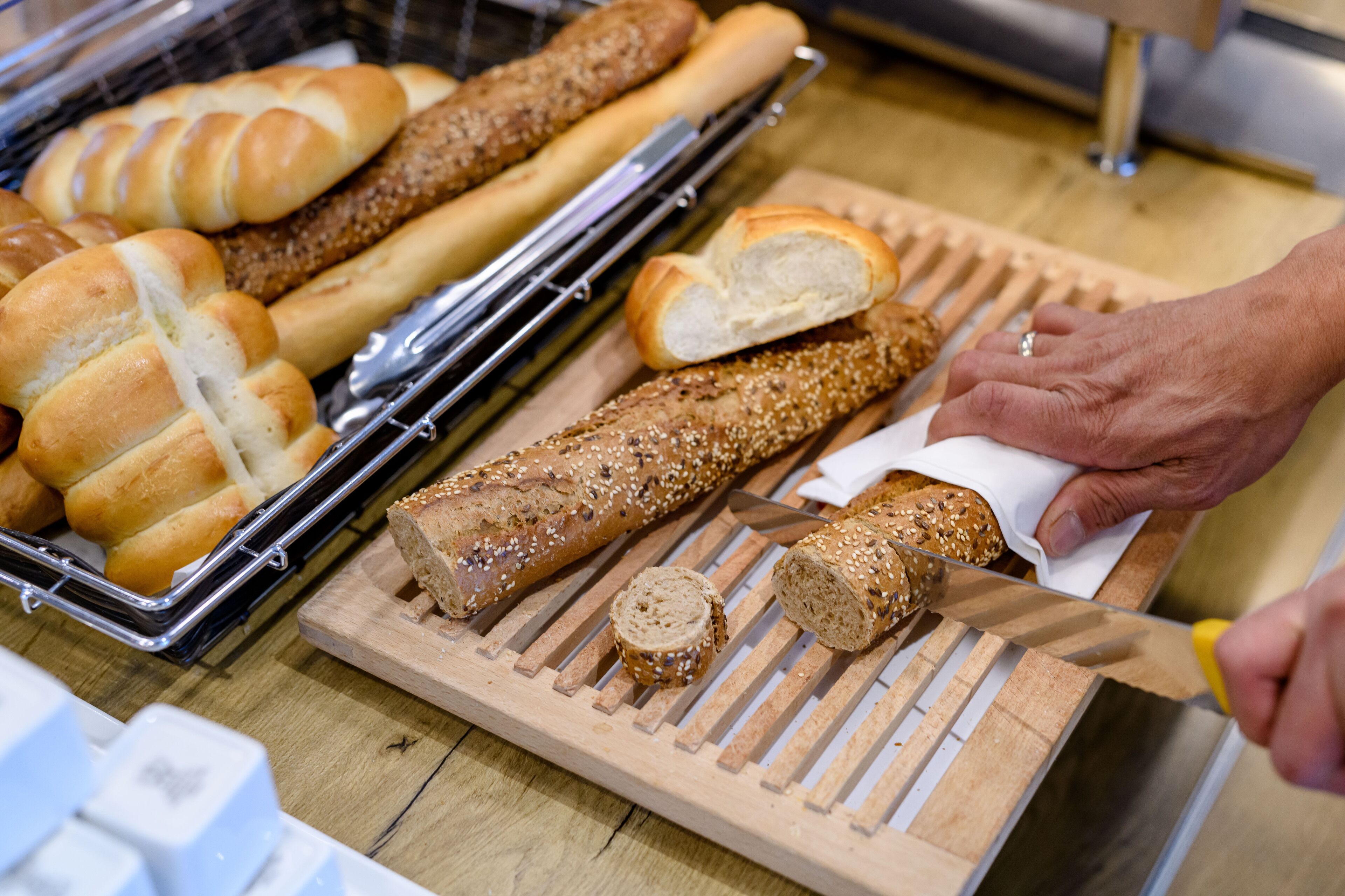 A variety of breads on a wooden cutting board with a knife cutting through one of them.