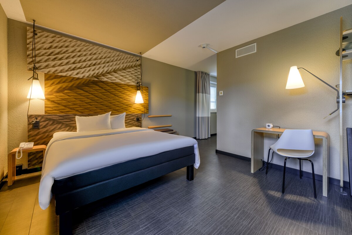 Une chambre d’hôtel comprenant un lit, un bureau, une chaise et deux lampes de chevet.