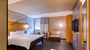 Une chambre d’hôtel avec un lit, un bureau, une chaise, une télévision et une fenêtre avec des rideaux.