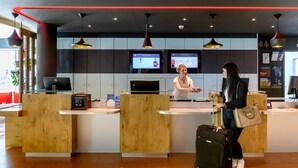 A reception desk with a wooden counter, a digital screen, and a security camera above. - ibis Zurich City West (Zürich)