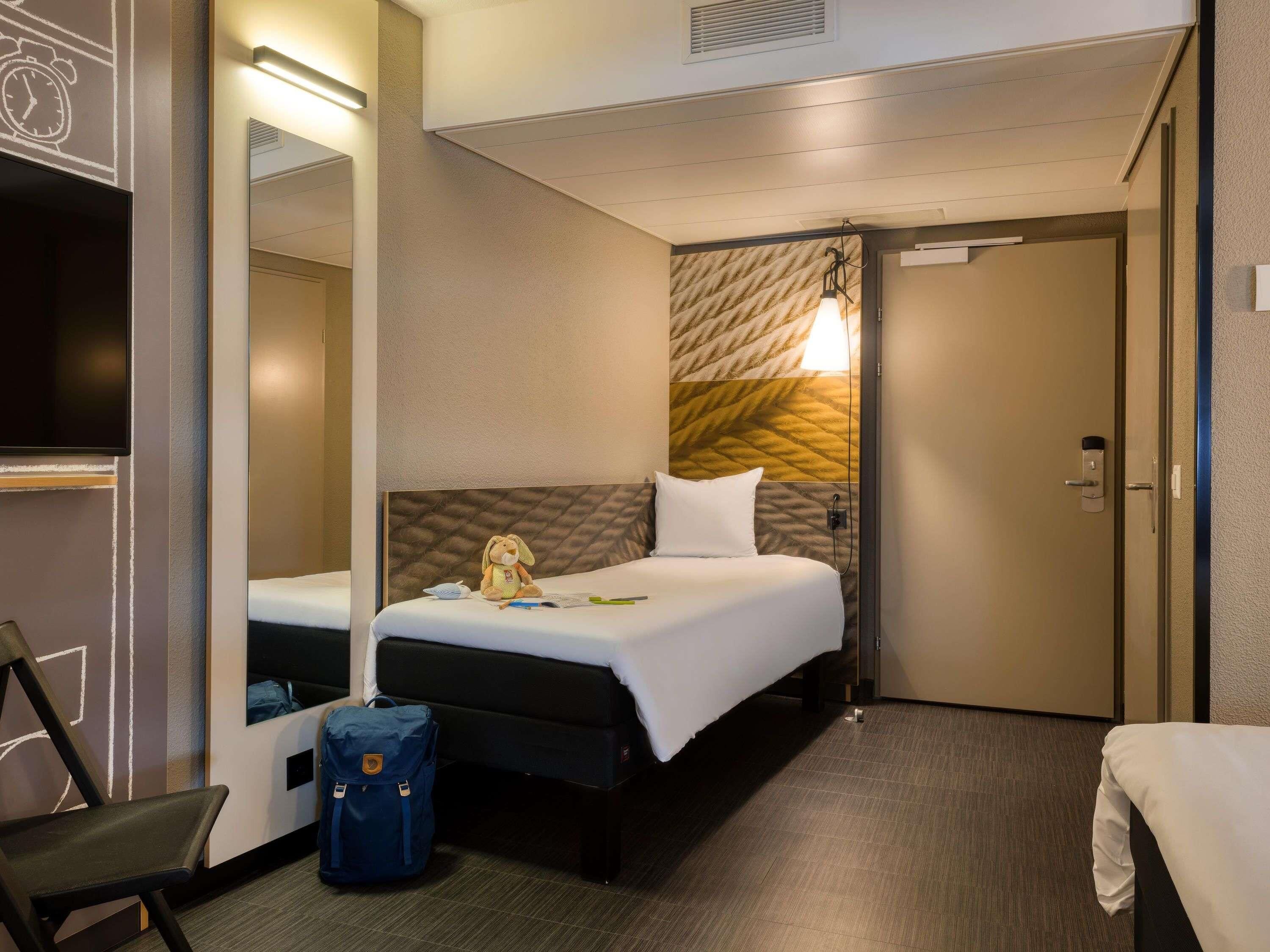 Een hotelkamer met een bed, een stoel, een bureau, een koffer en een spiegel.