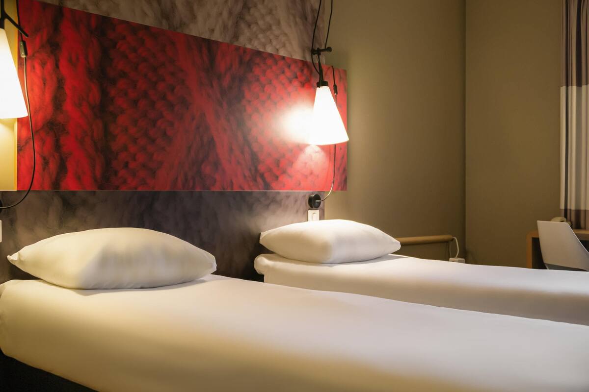Ein Hotelzimmer mit zwei Betten, einer roten, strukturierten Wand und zwei Pendelleuchten.