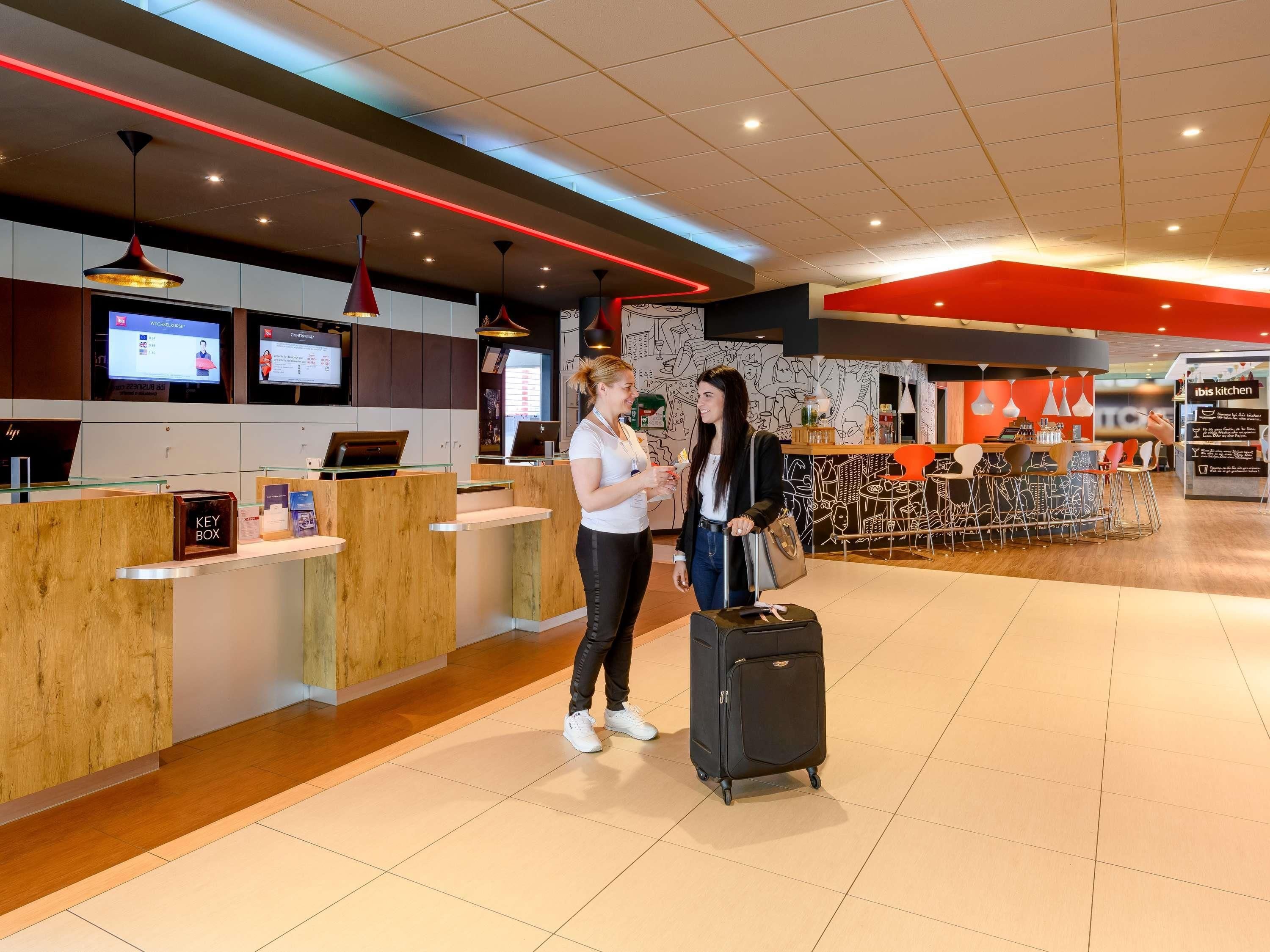 A modern hotel lobby with a reception desk, digital screens, and a casual seating area.