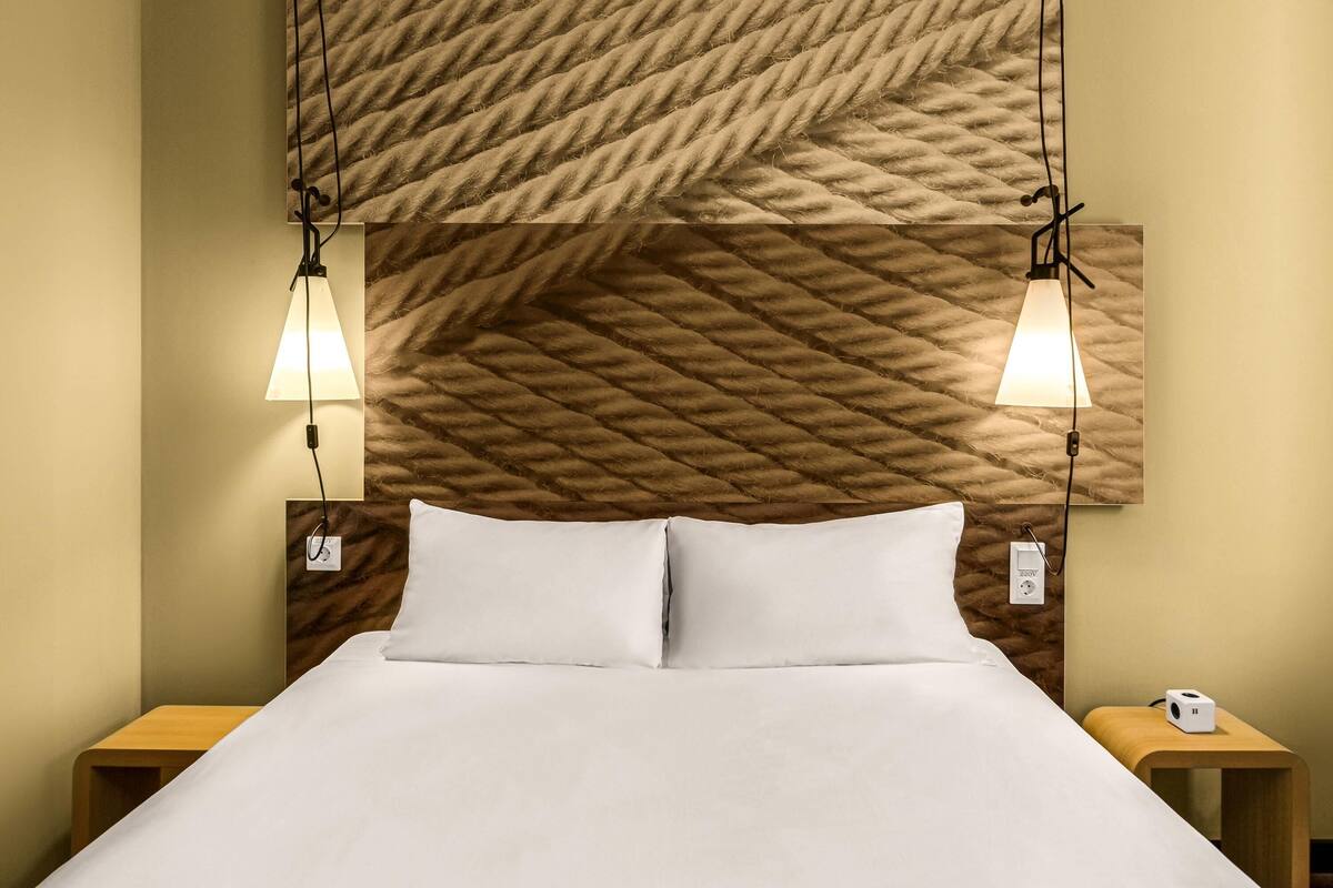 Ein Hotelzimmer mit einem Bett, zwei Nachttischen, einem Kopfteil mit strukturierter Musterung und zwei Wandlampen.