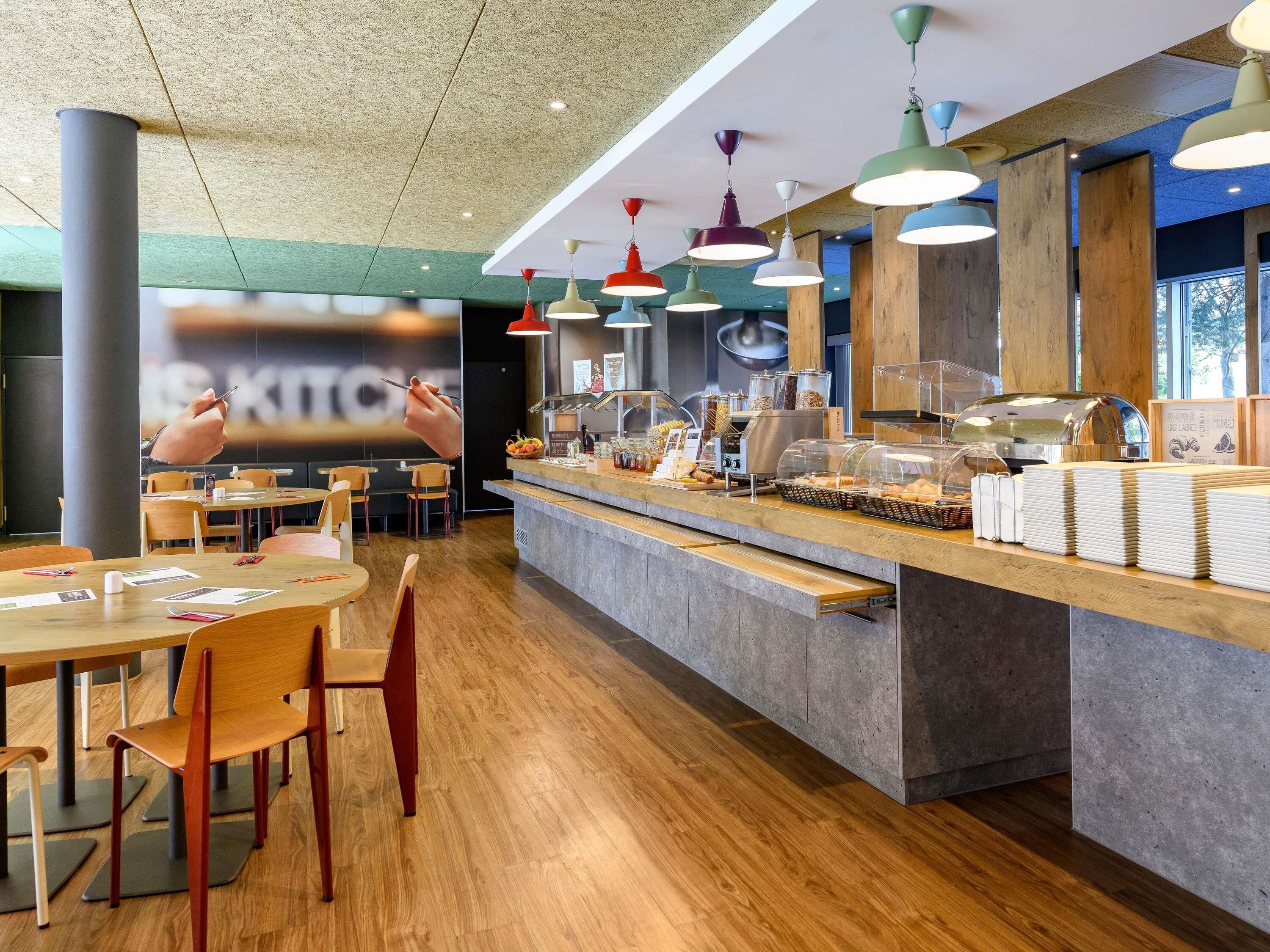 A modern cafe interior with wooden tables, chairs, and a counter with food items.