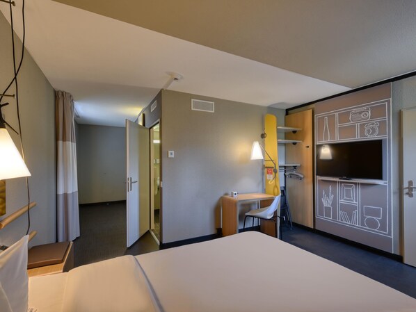 Habitación de hotel con cama, escritorio, silla, televisor y armario.