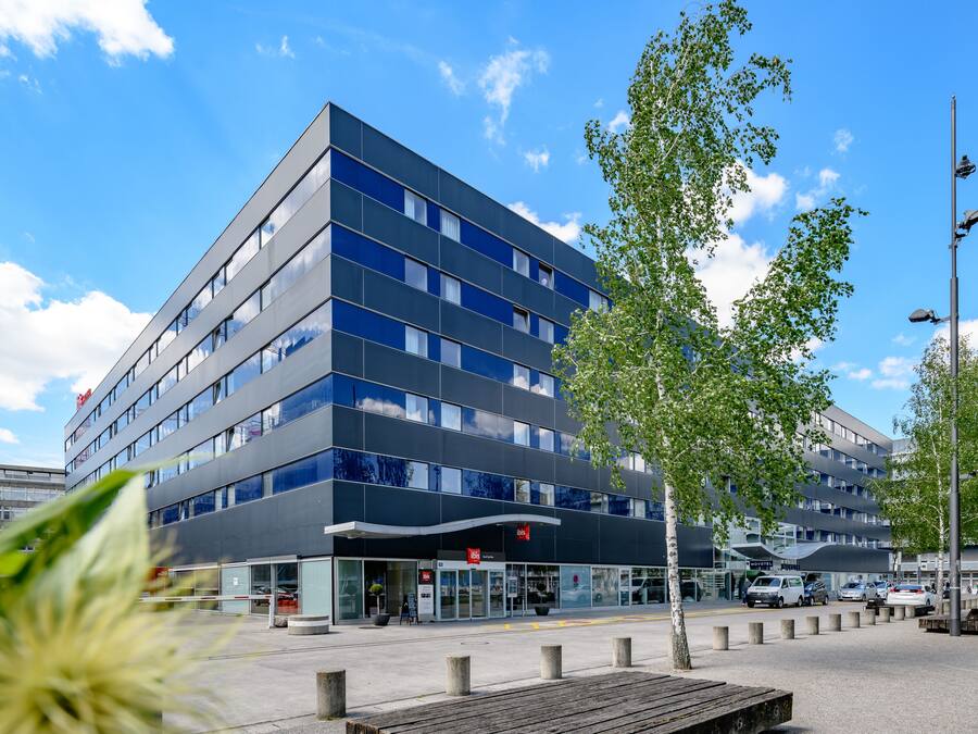 A modern hotel with a glass facade, multiple floors, and a parking area with cars.