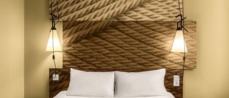 A hotel room with a bed, two bedside tables, a headboard with a textured pattern, and two wall-mounted lamps.
