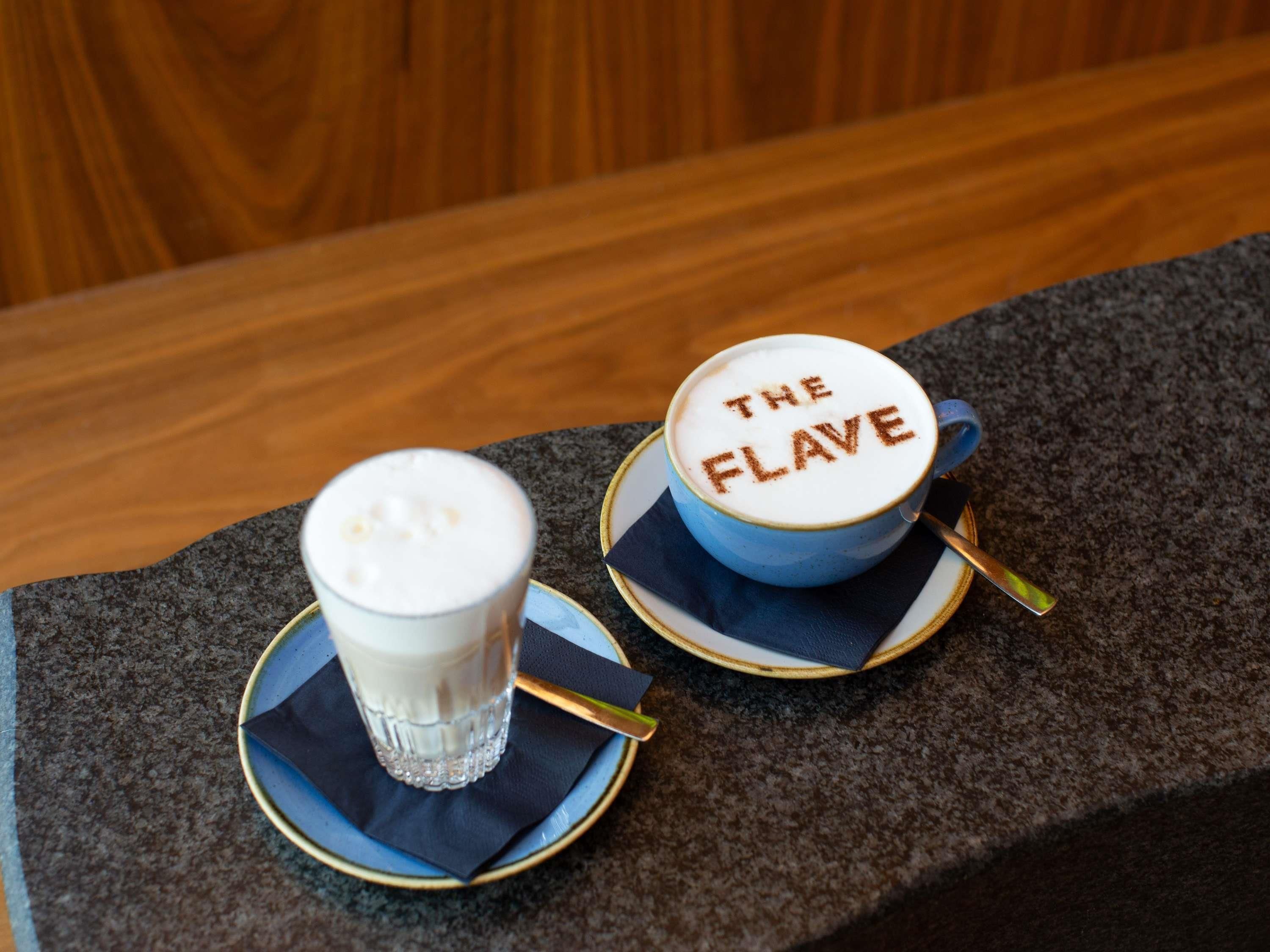 Deux tasses de café, posées sur des soucoupes avec des serviettes et des cuillères, dont l’une est étiquetée « THE FLAVE ».