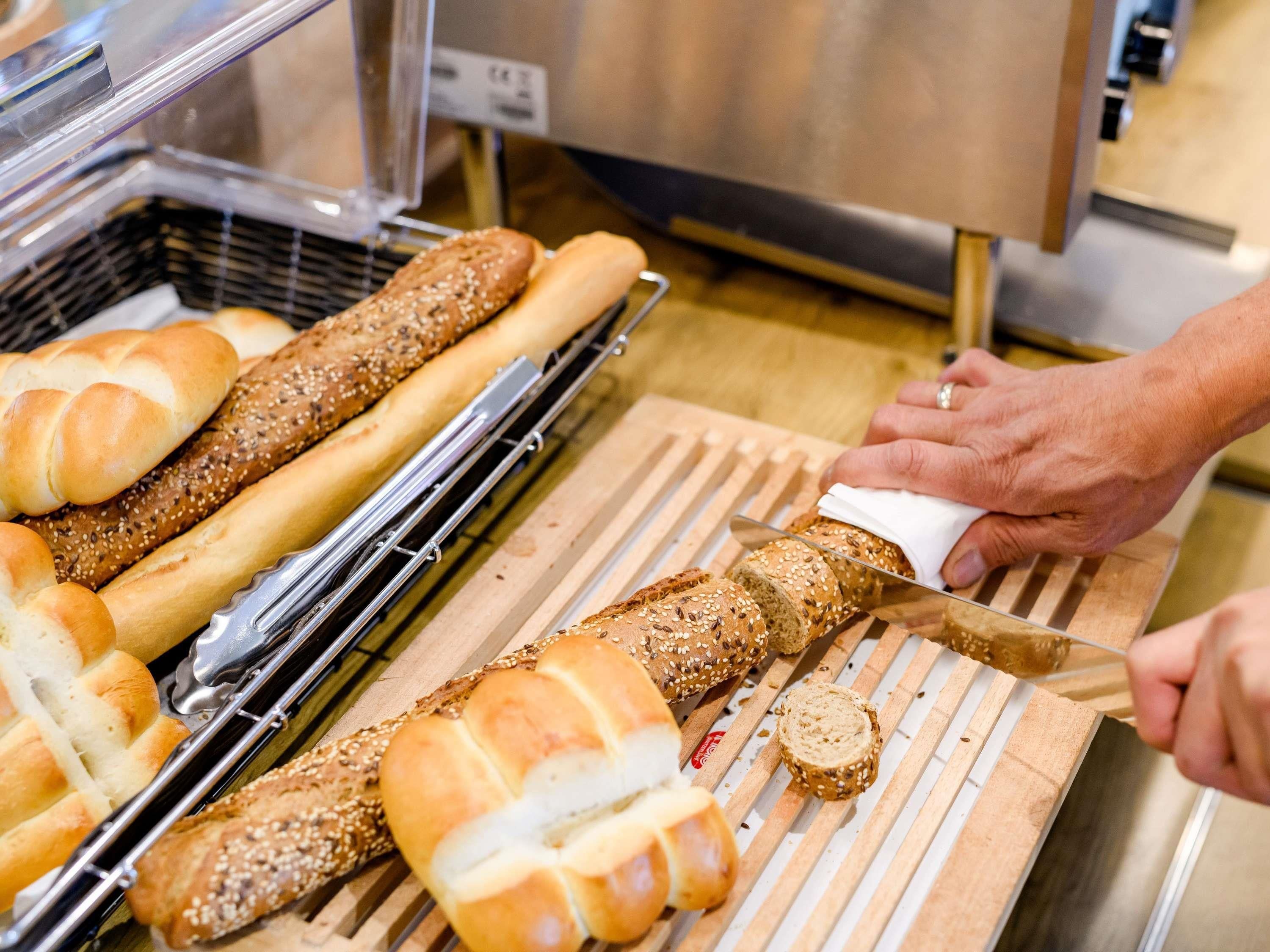 A bakery with various loaves of bread on display and a person slicing a loaf.
