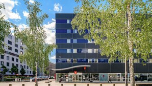Un bâtiment moderne à la façade sobre, doté de grandes fenêtres et d’une entrée imposante avec une enseigne rouge.