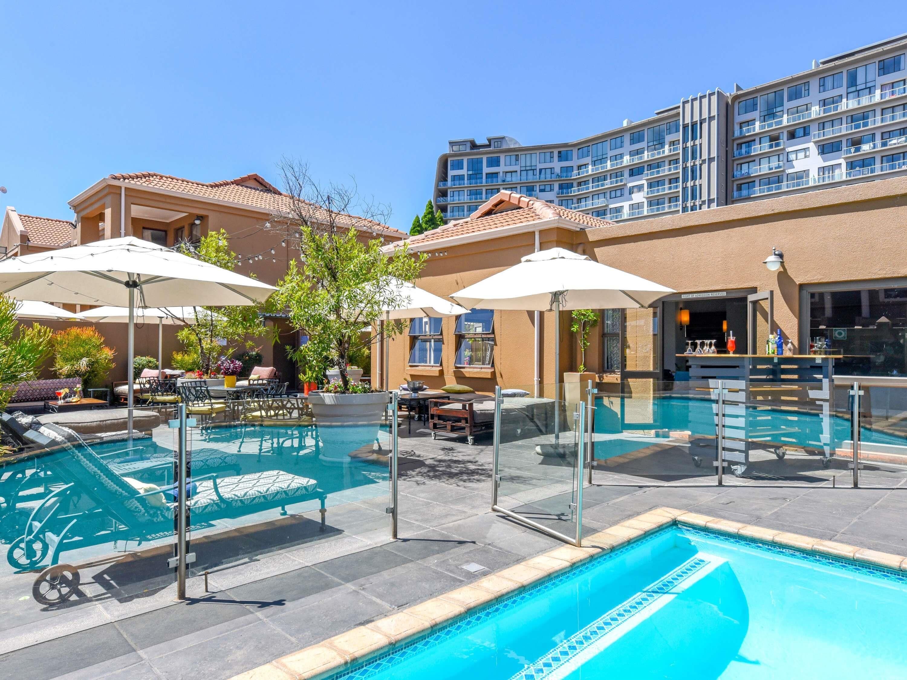 Una piscina al aire libre, sombrillas, sillones reclinables de piscina