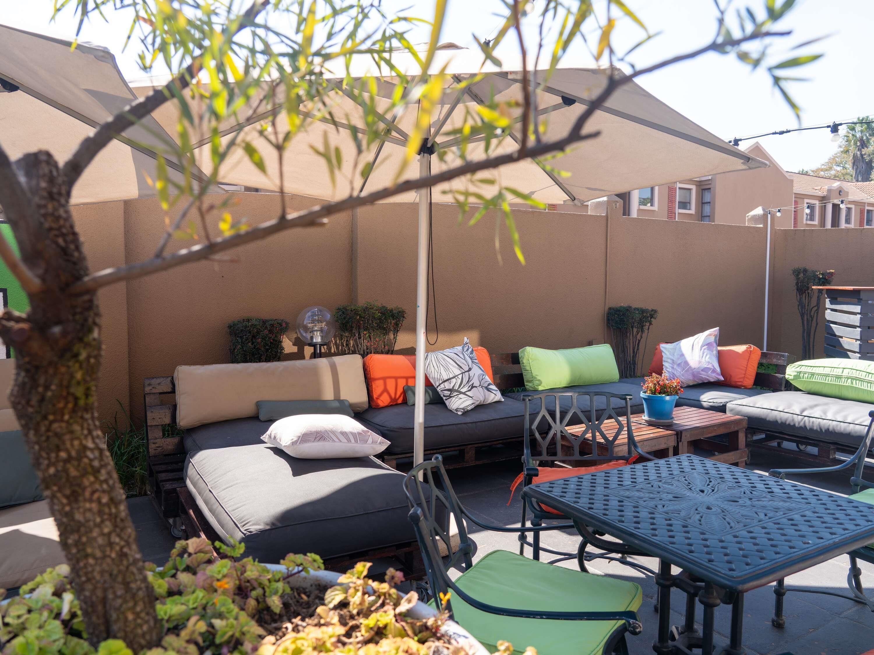 An outdoor seating area with a sofa, chairs, and a table, surrounded by plants and a tree.