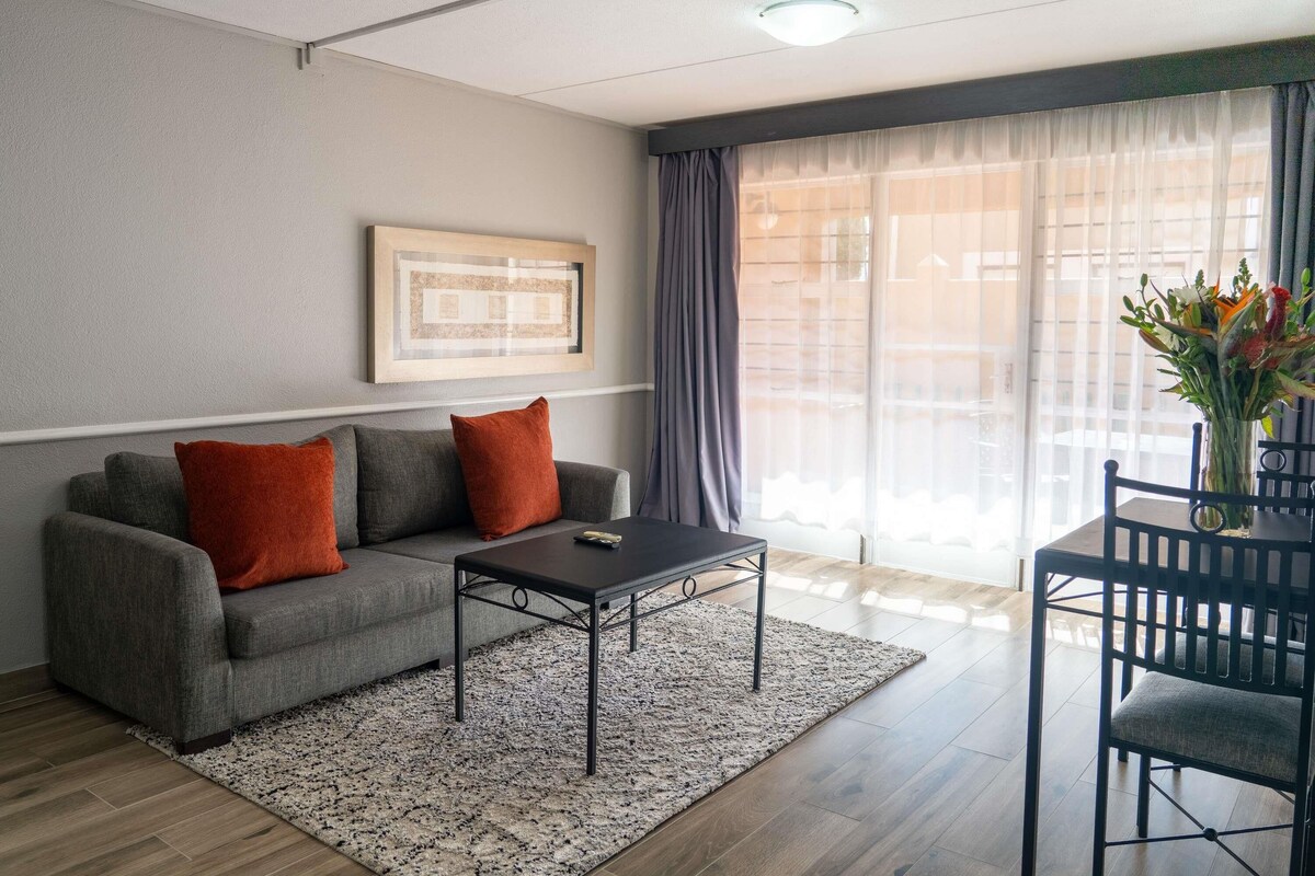 A living room with a grey sofa, a coffee table, and a dining table with chairs.