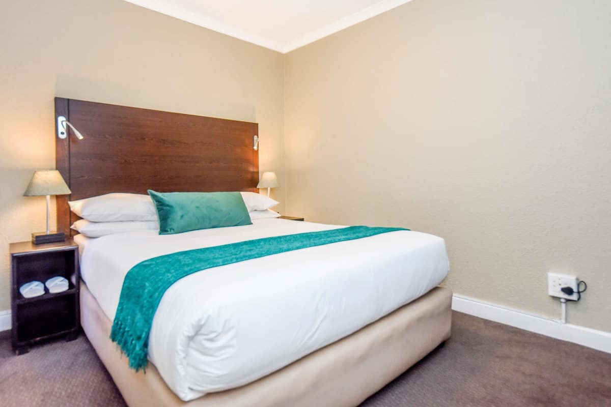 A neatly made bed with a wooden headboard, two bedside lamps, and a green throw blanket.