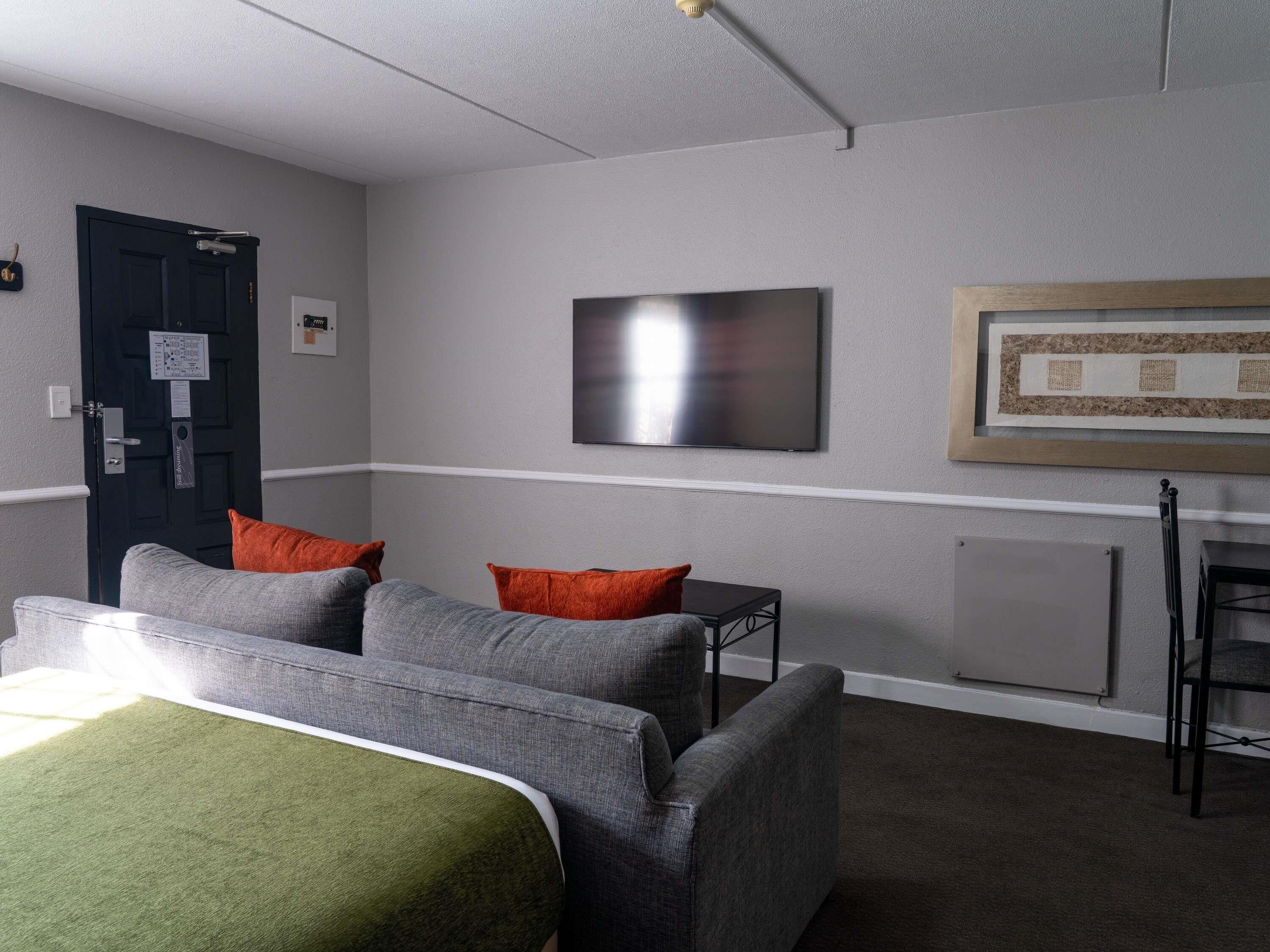 Een hotelkamer met een bed, twee fauteuils, een kleine tafel, een flatscreen televisie, een lijst met een afbeelding en een deur met een bordje.