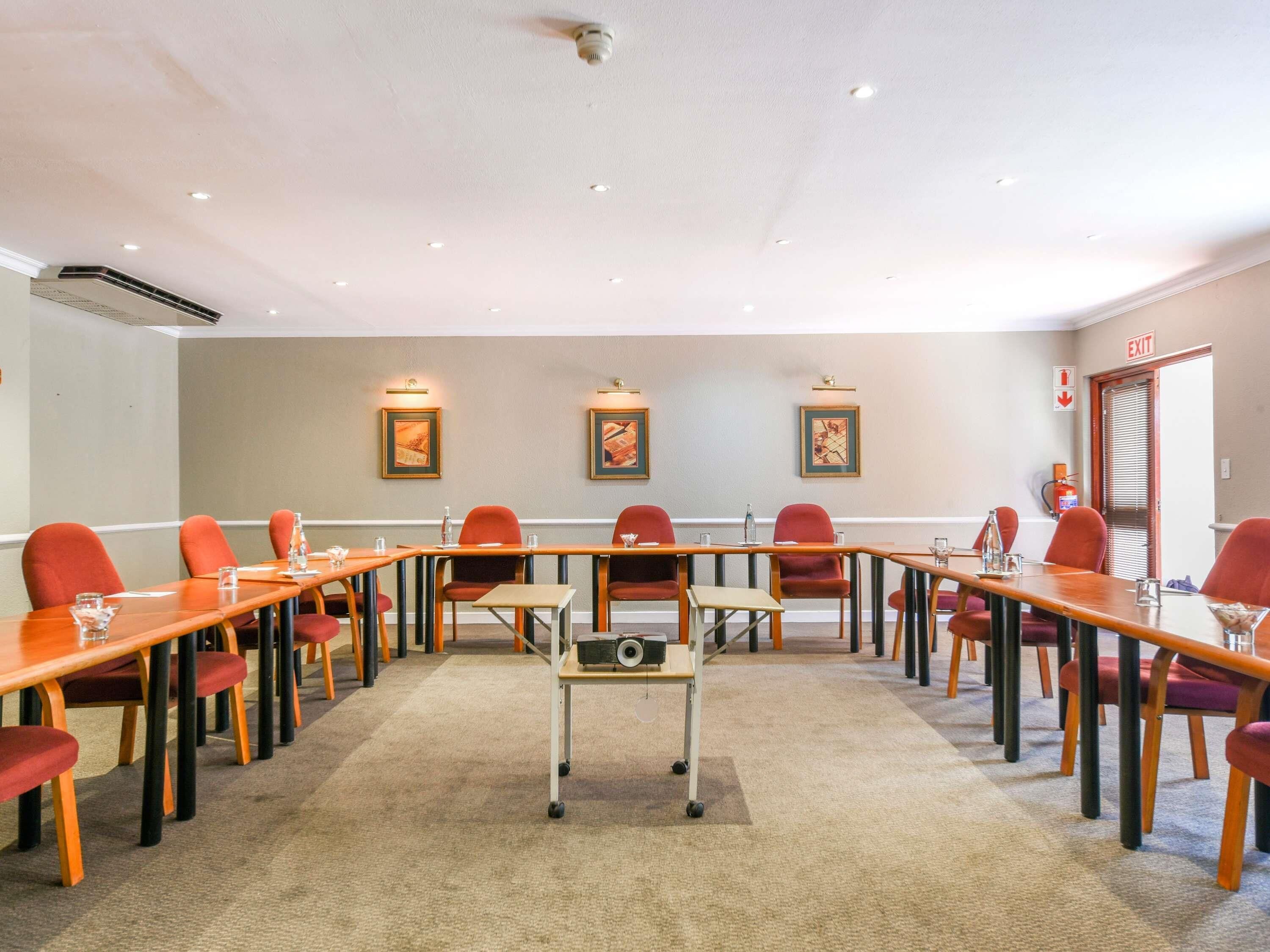 A conference room with long tables, red chairs, and framed artwork on the walls.
