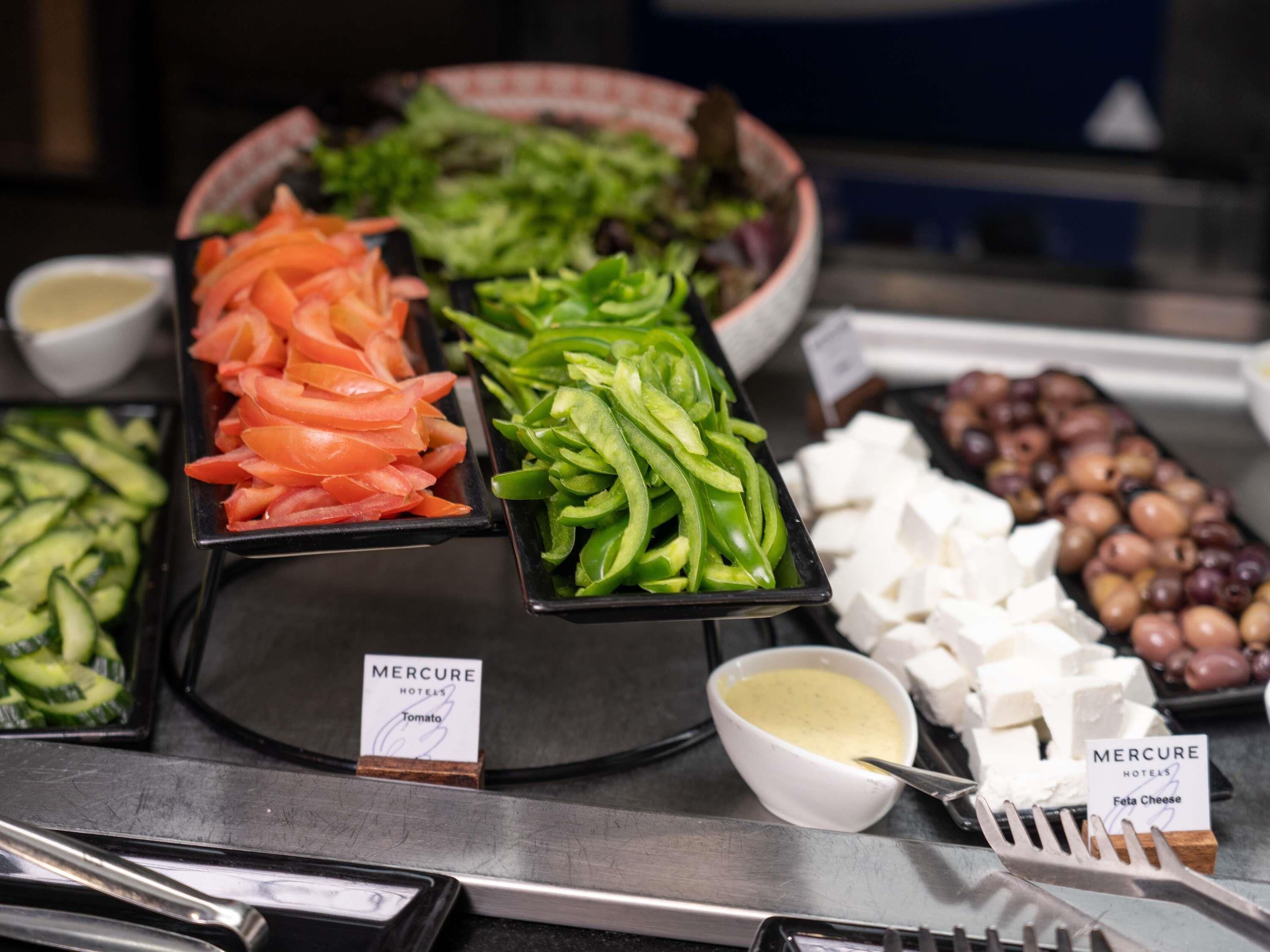 Un buffet proposant une variété de plats, notamment des légumes coupés en tranches, du fromage feta et des olives.