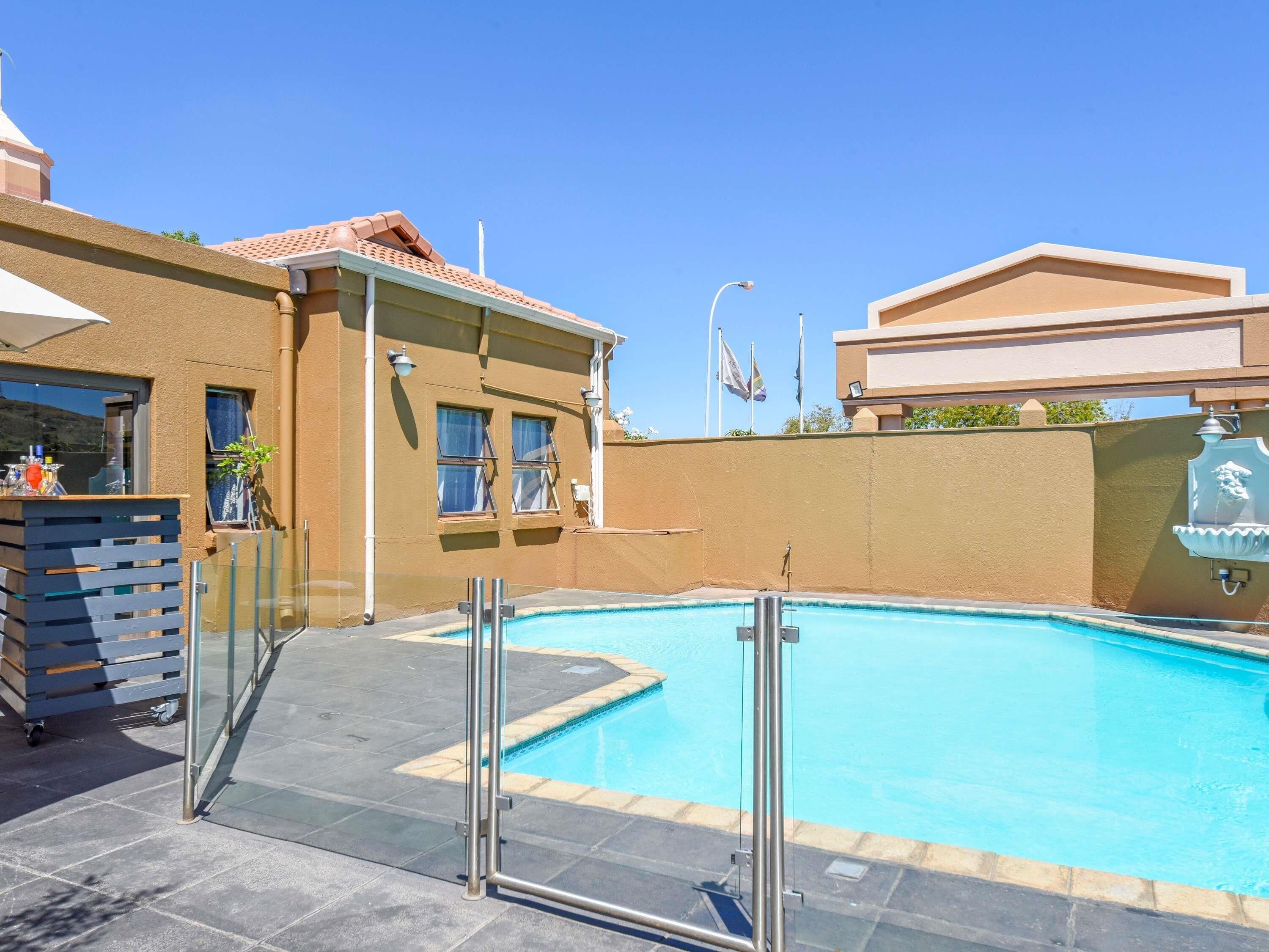 A swimming pool with a glass barrier, a bar area with a drink dispenser, and a building with a tiled roof.