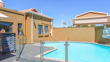 A swimming pool with a glass barrier, a bar area with a drink dispenser, and a building with a tiled roof.