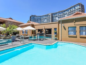 A hotel with a swimming pool, outdoor seating, and a modern building in the background. - Mercure Johannesburg Bedfordview Hotel (Germiston)