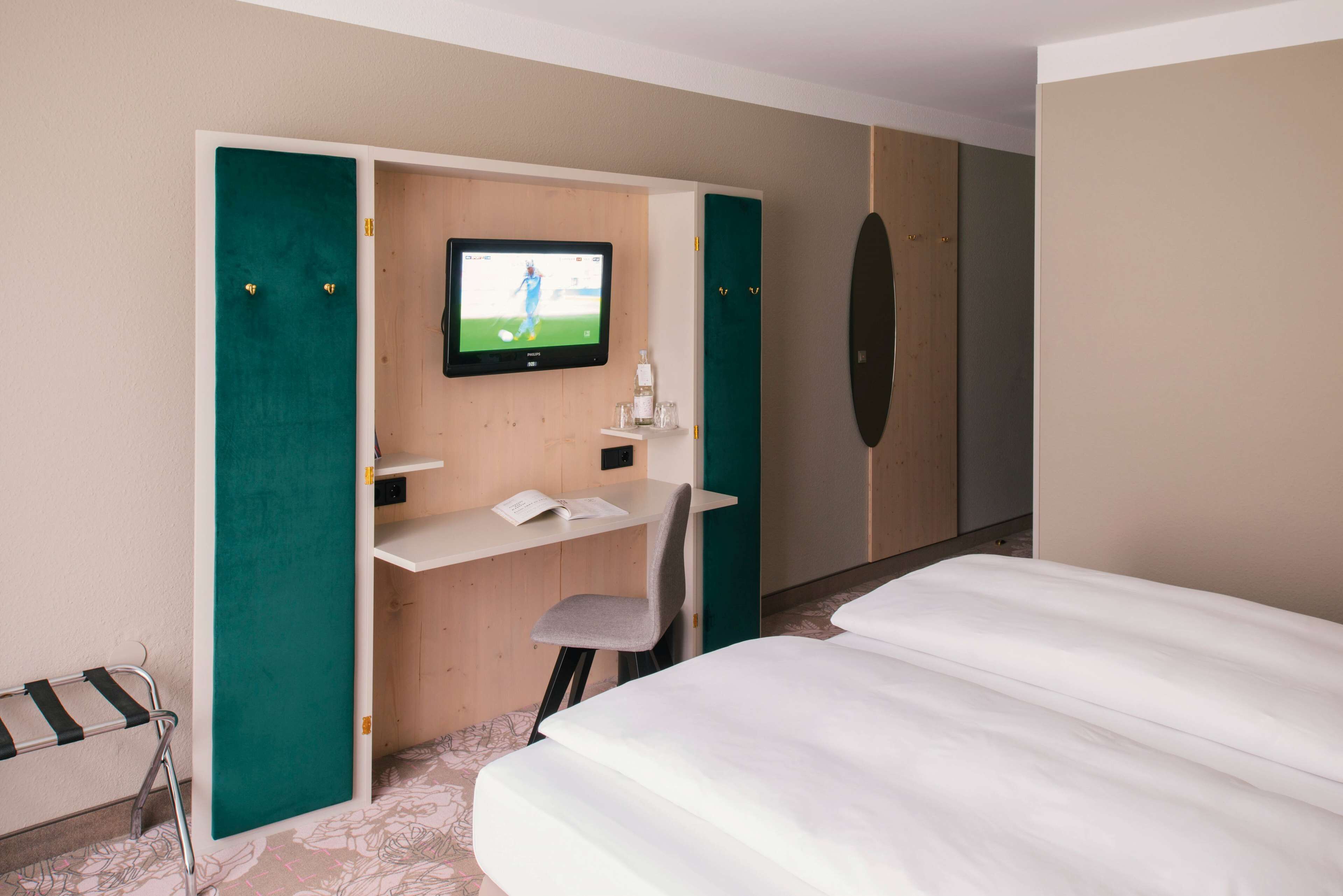 Ein Hotelzimmer mit einem Bett, einem Schreibtisch mit Stuhl, einem Fernseher und einem Kleiderschrank.