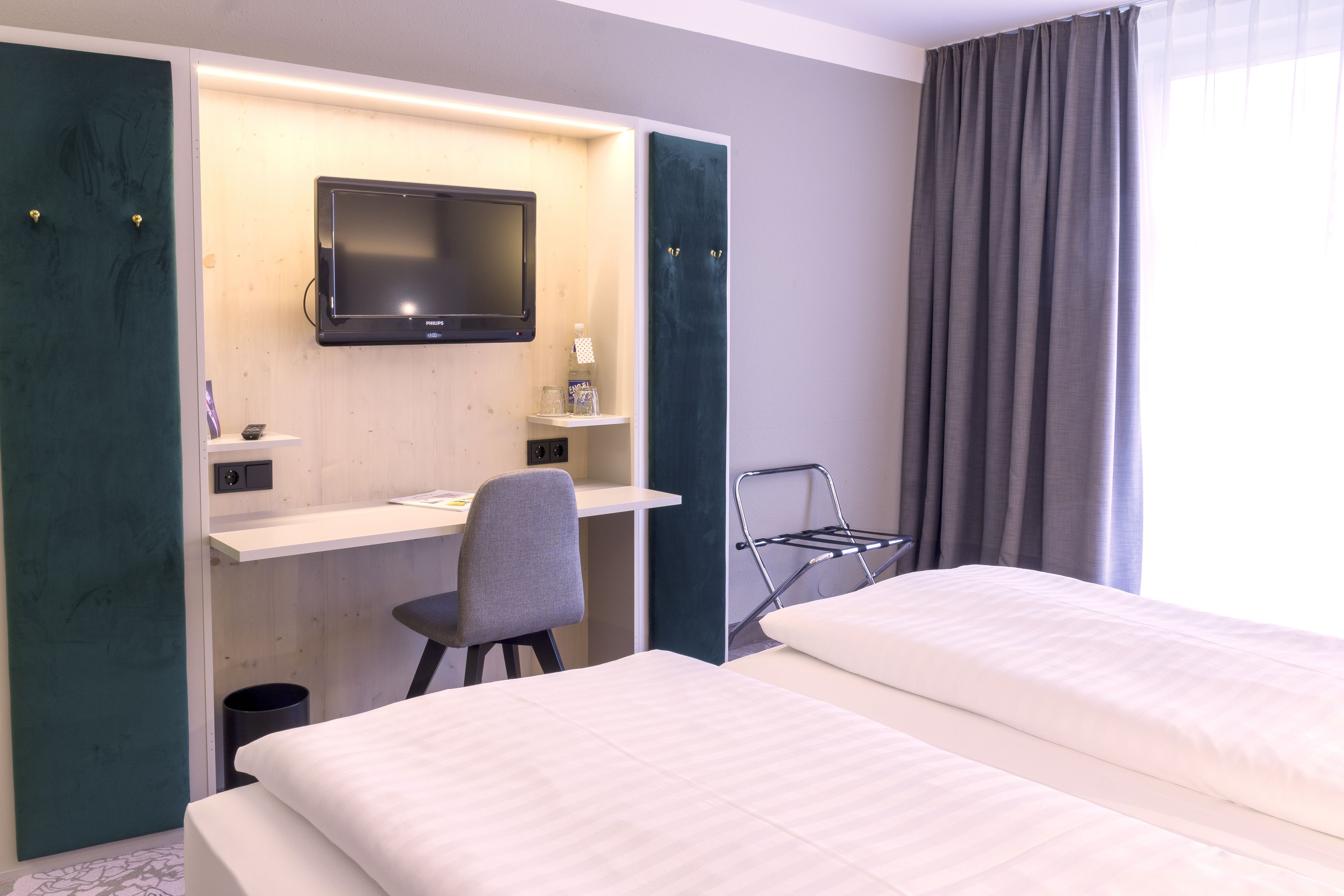 Ett hotellrum med två sängar, ett skrivbord med en stol, en TV och ett fönster med gardiner.