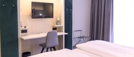 Habitación de hotel con dos camas, un escritorio con silla, televisión y ventana con cortinas.