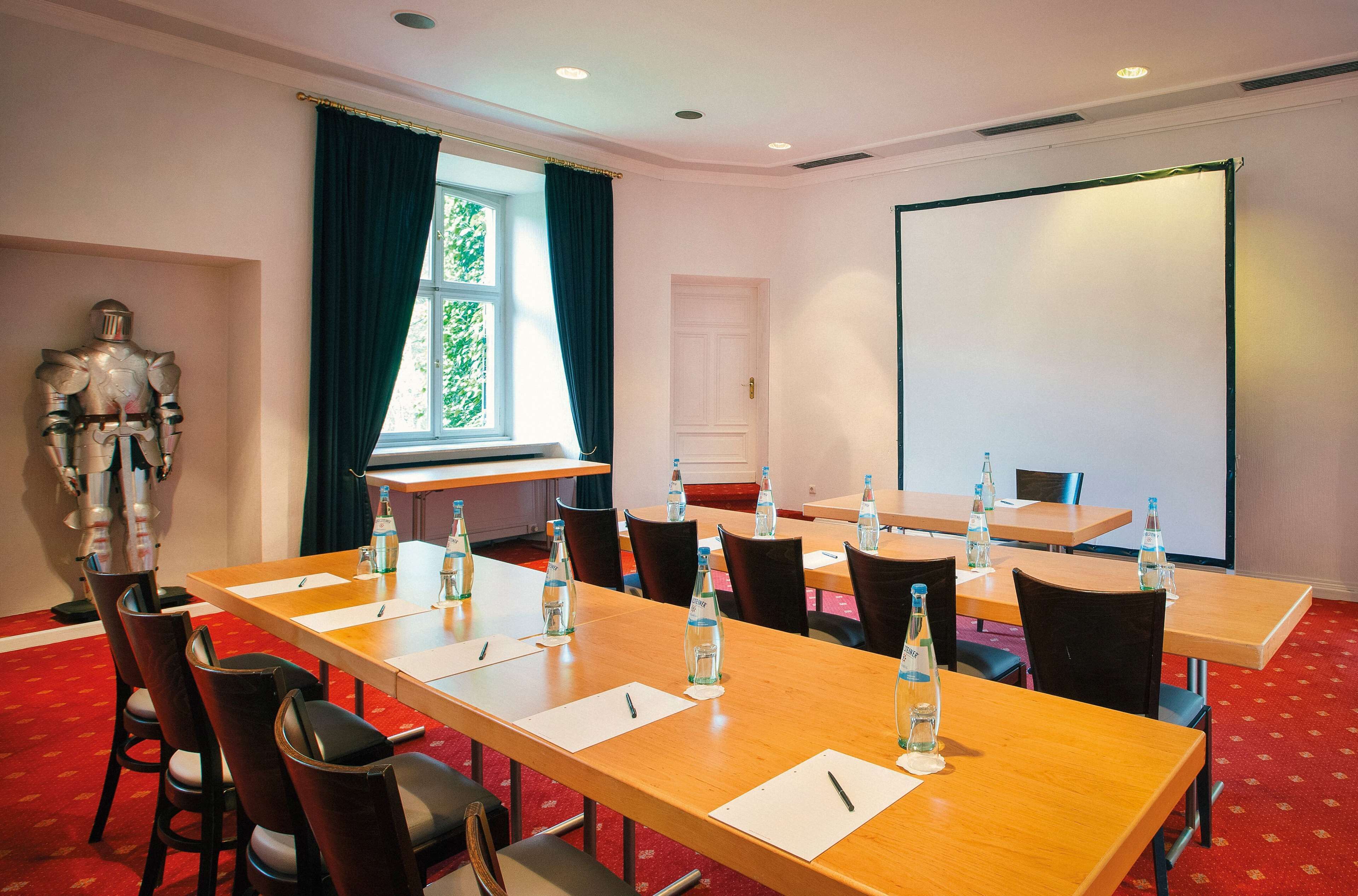 A conference room with a long table, chairs, water bottles, and a projector screen.