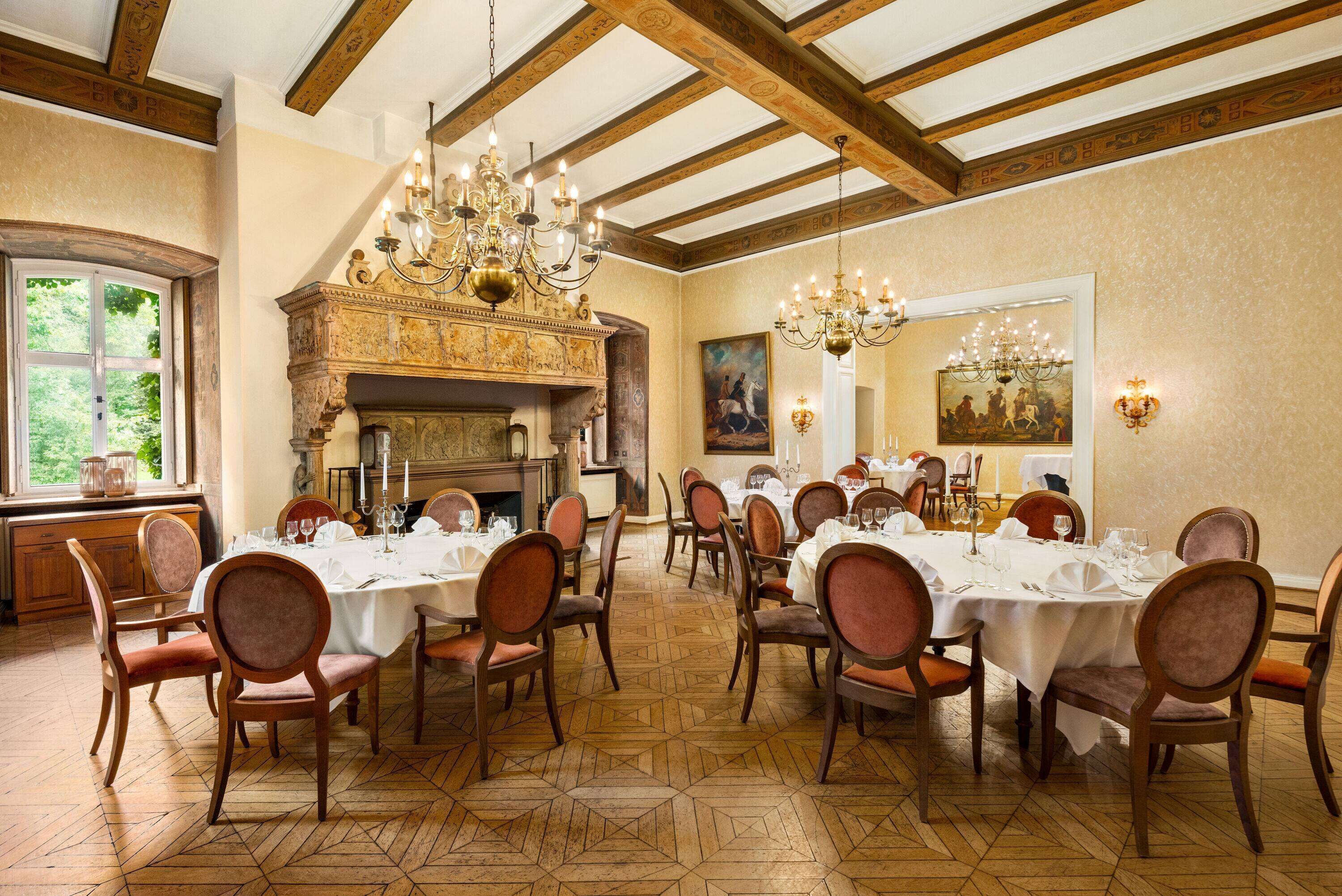 A dining room with wooden chairs and tables, a fireplace, and chandeliers.