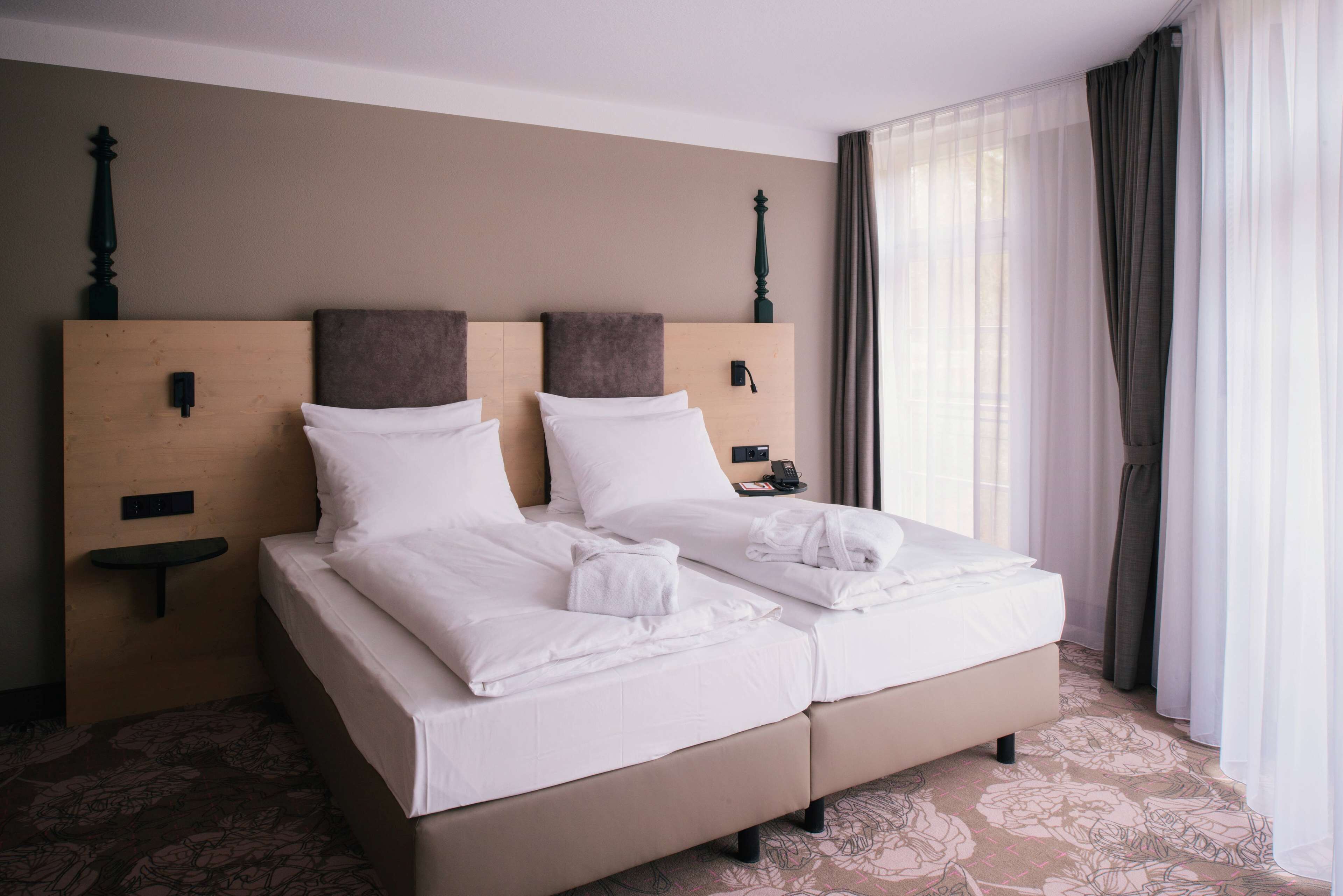 A double bed with white linens, a wooden headboard, and a bedside table with a phone and a lamp.