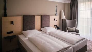 A hotel room with a large bed, a chair, a lamp, and a window with curtains.
