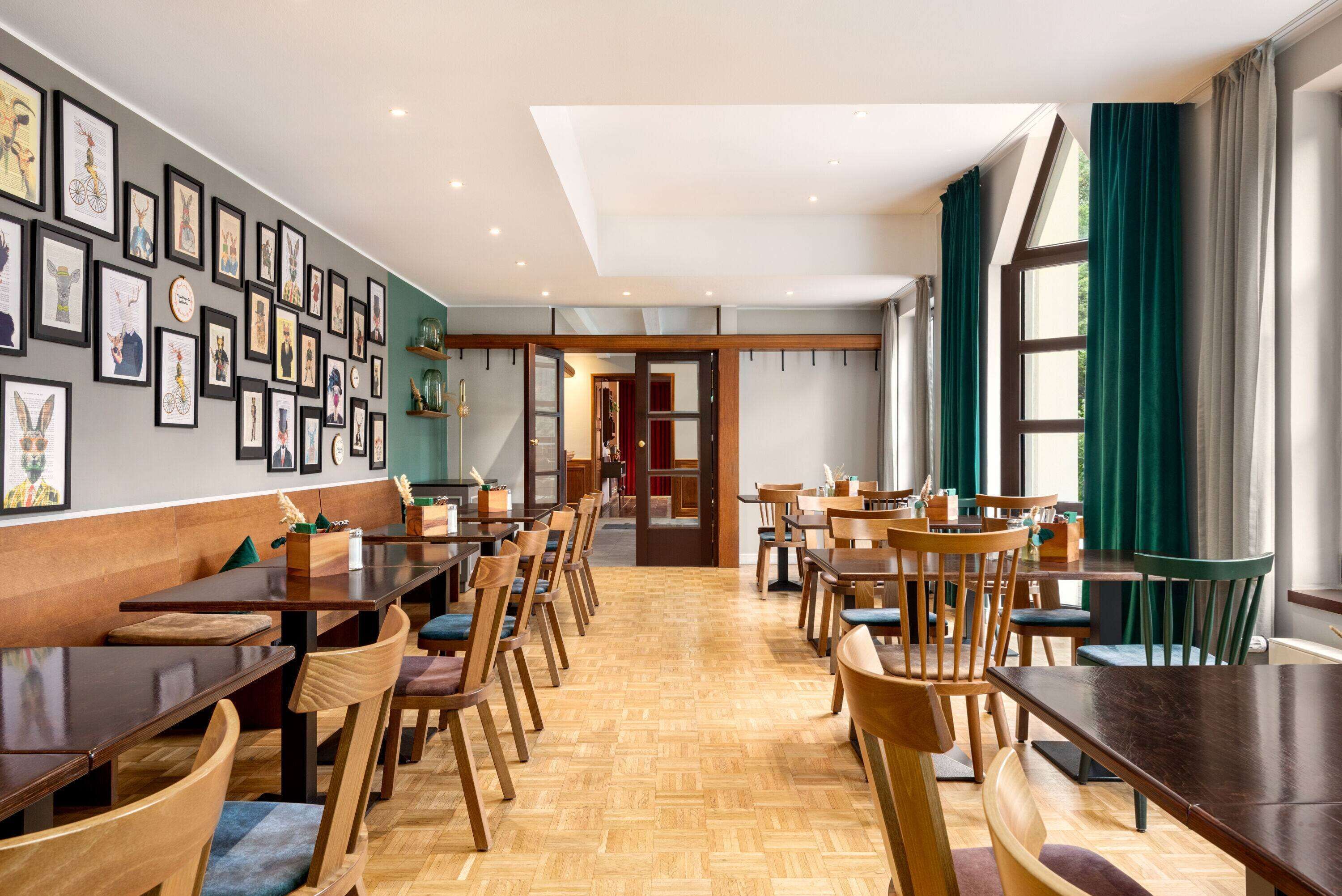 Un comedor amplio con mesas y sillas de madera, obras de arte en las paredes y ventanas grandes con cortinas.