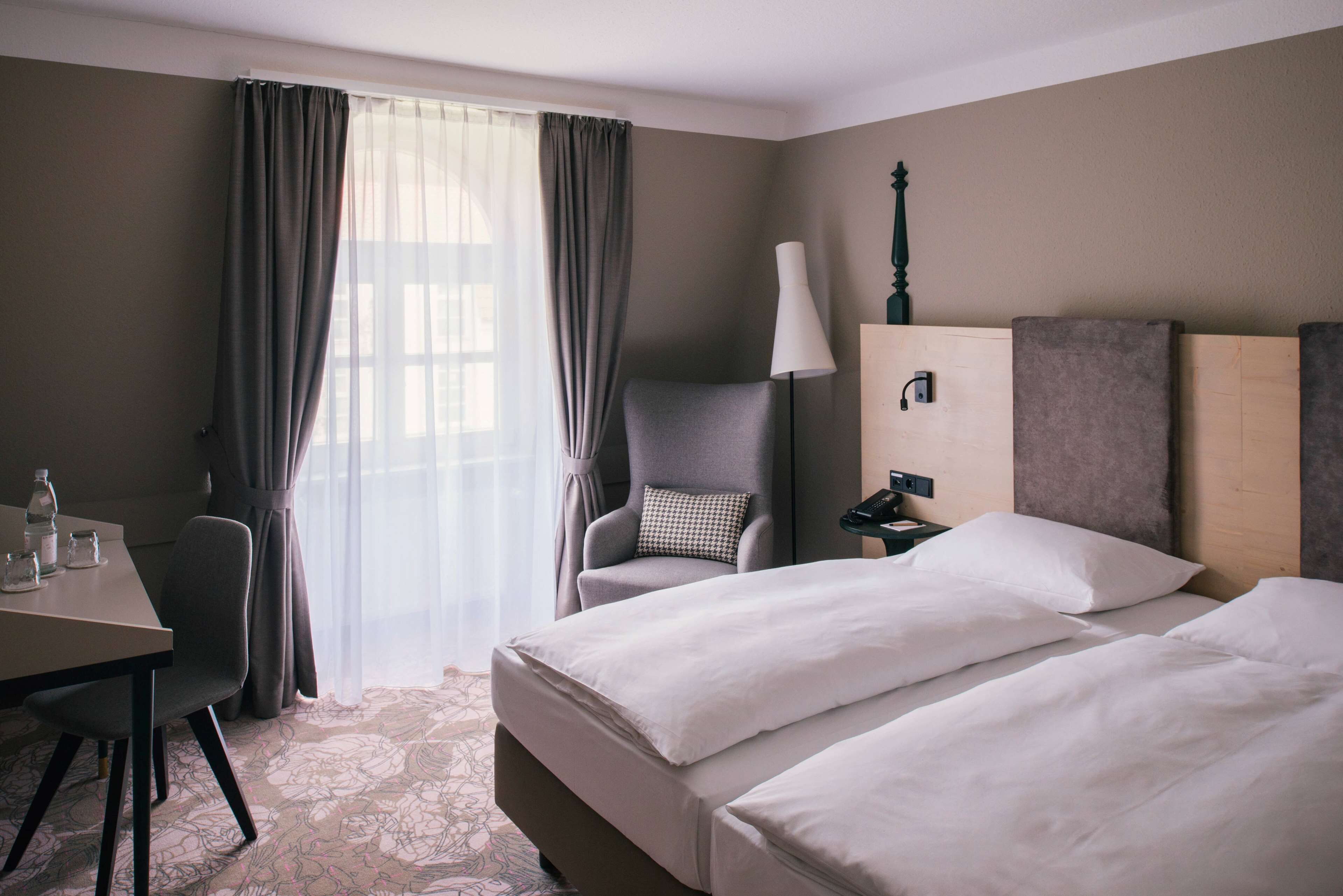 A hotel room with two beds, a desk, a chair, a lamp, and a nightstand.