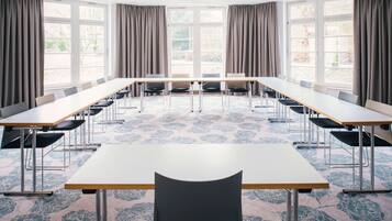 Uma sala de conferências com uma mesa comprida, várias cadeiras e janelas amplas com cortinas.