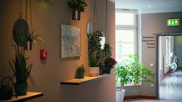 Zona de recepción con mostrador, plantas en macetas, un espejo y una obra de arte enmarcada.