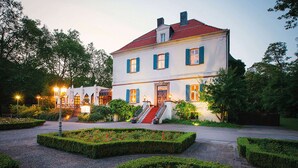 Un bâtiment à deux étages, doté d’un toit recouvert de tuiles rouges, d’un escalier central et d’un jardin bien entretenu agrémenté de haies et de parterres de fleurs.