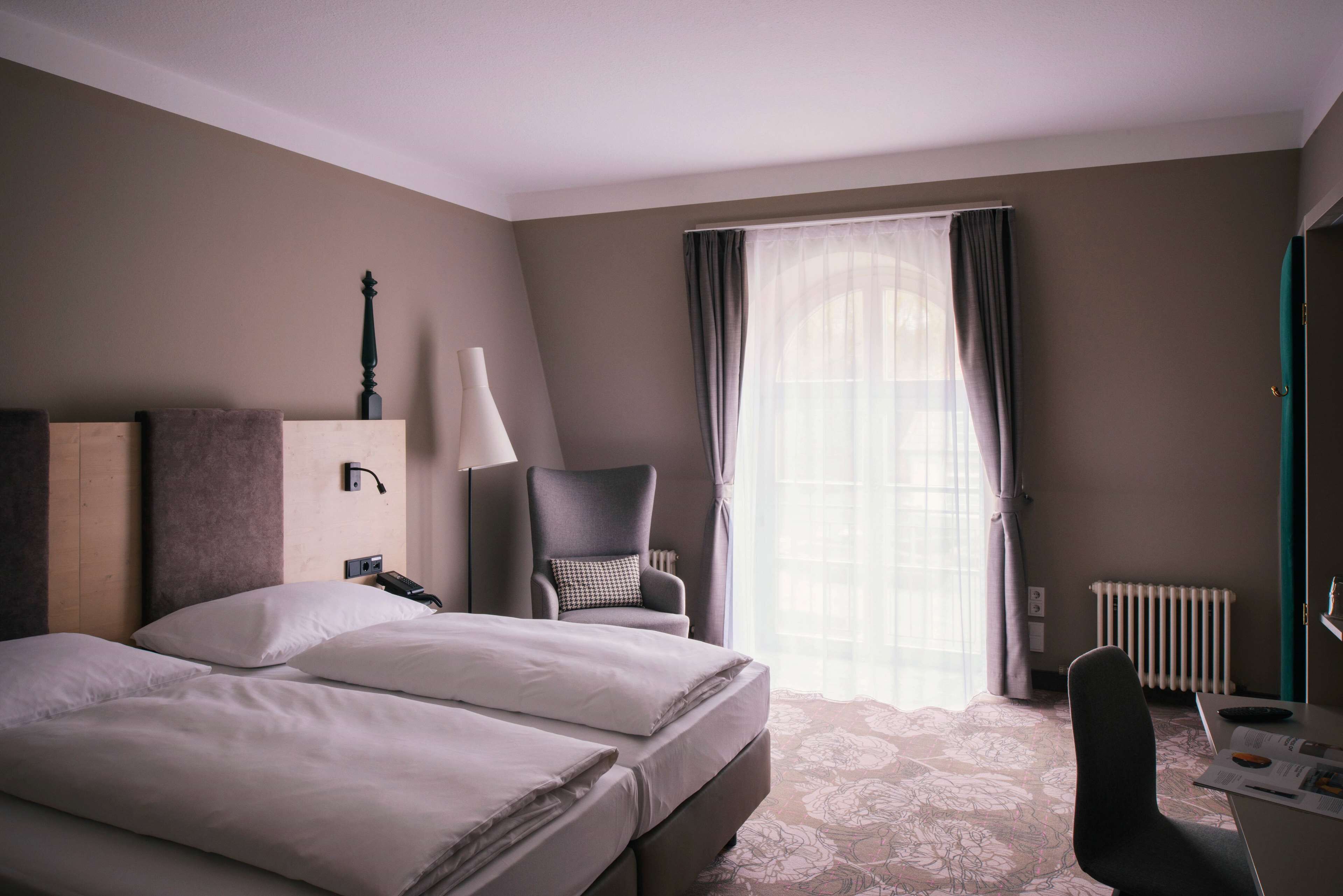 A hotel room with two beds, a chair, a desk, and a window with curtains.