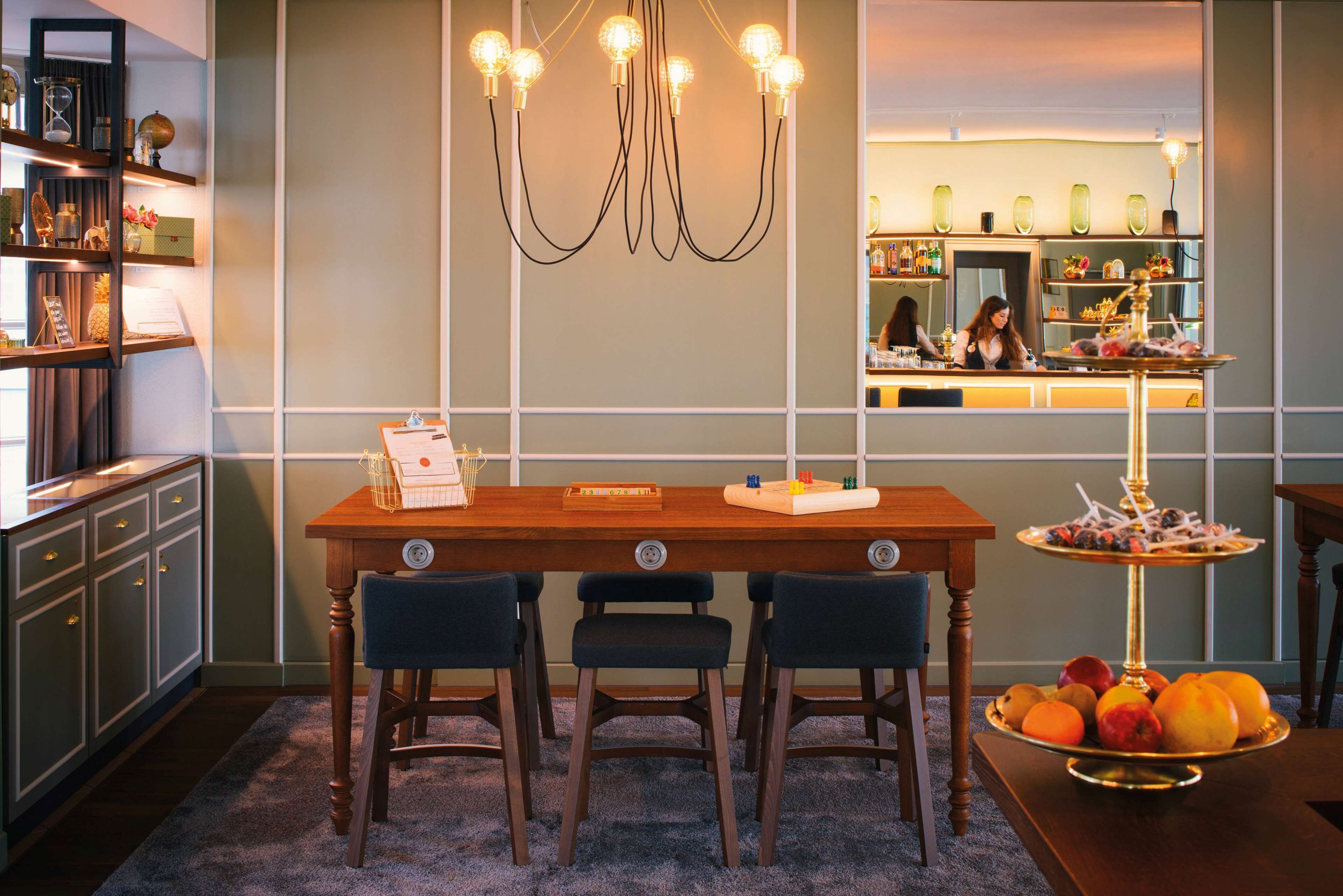Un coin repas avec une table en bois, trois chaises, un lustre et une corbeille de fruits.