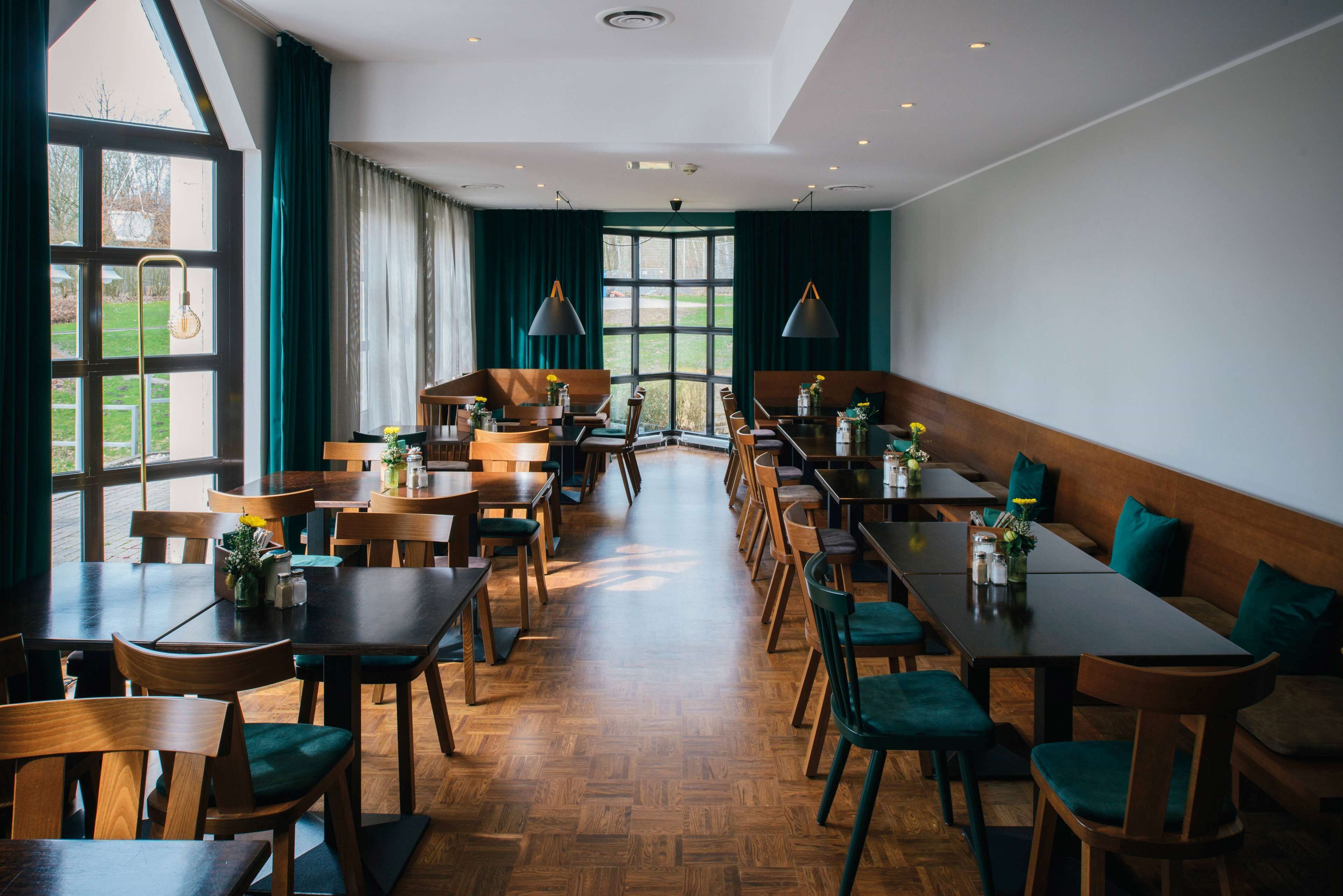 A spacious dining area with multiple tables and chairs, large windows with curtains, and pendant lighting.
