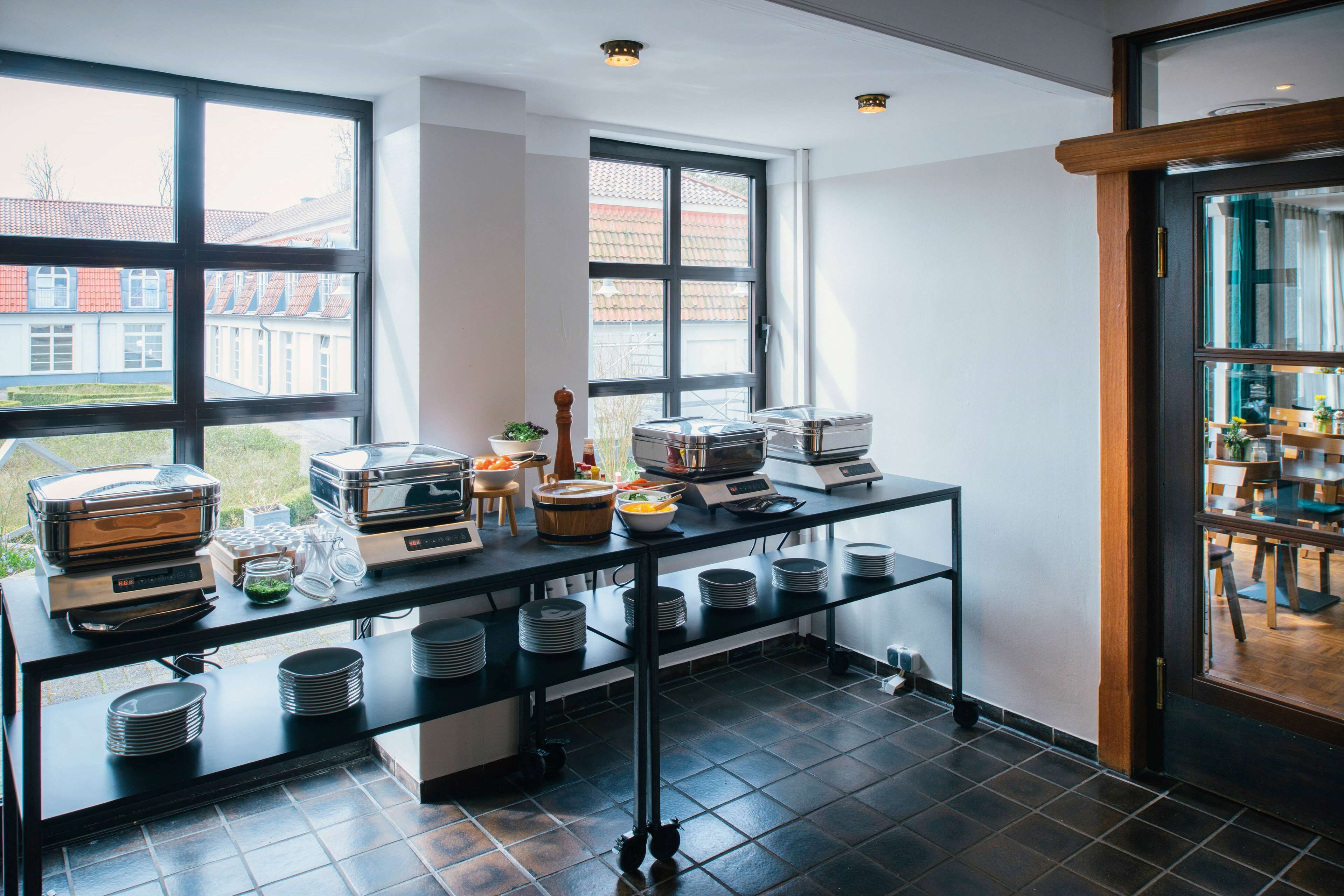 Ein reichhaltiges Buffet mit verschiedenen Speisebehältern, Serviergeschirr, einer Kaffeemaschine und einer kleinen Pflanze.