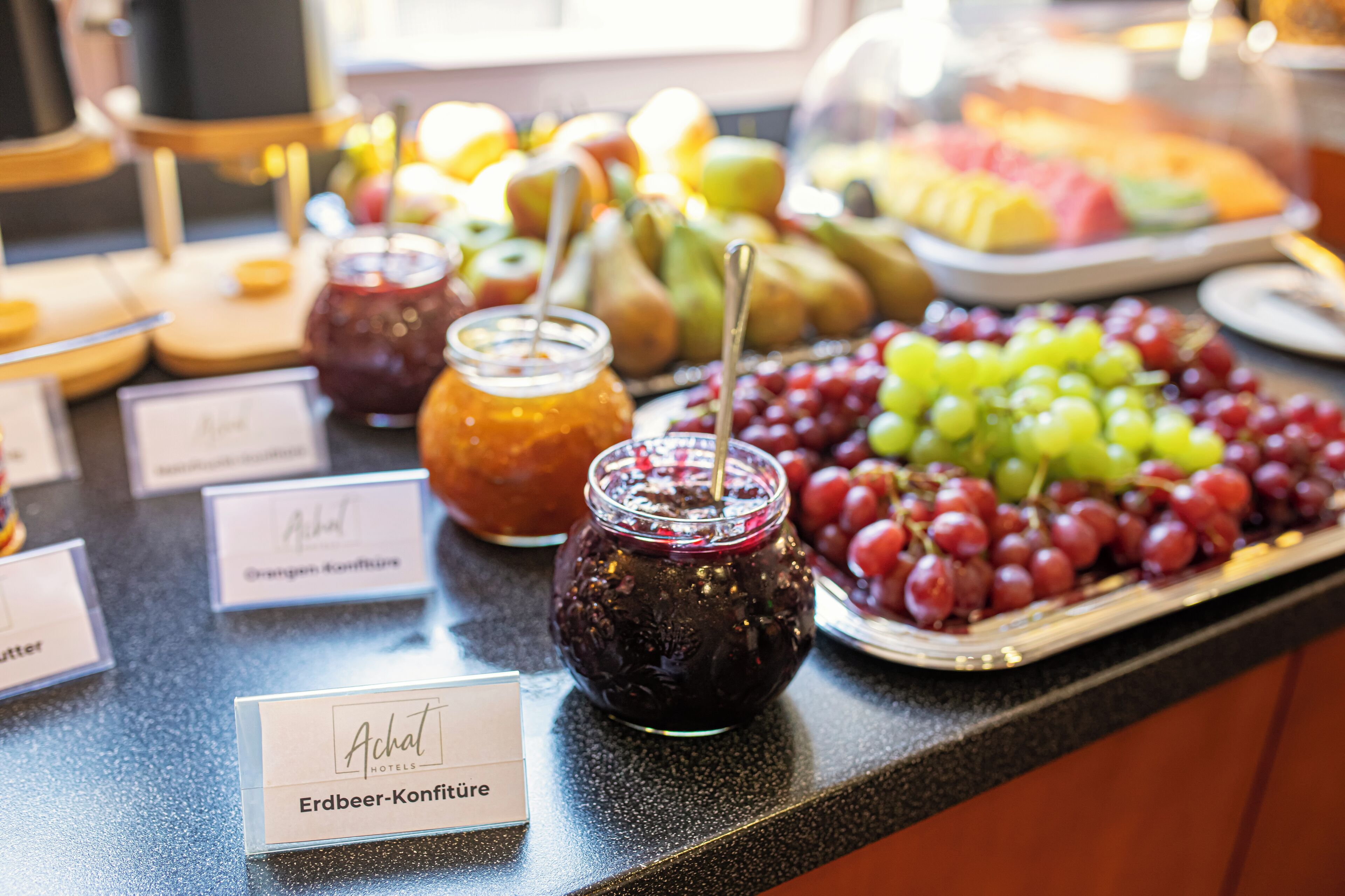 A buffet table with various fruits, jams, and a sign for 'Achat Hotels'.