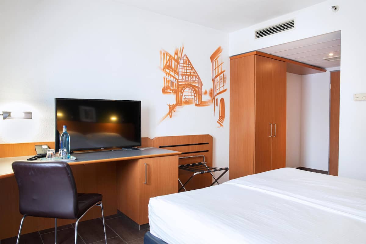 A hotel room with a bed, a desk with a chair, a television, and a wardrobe.