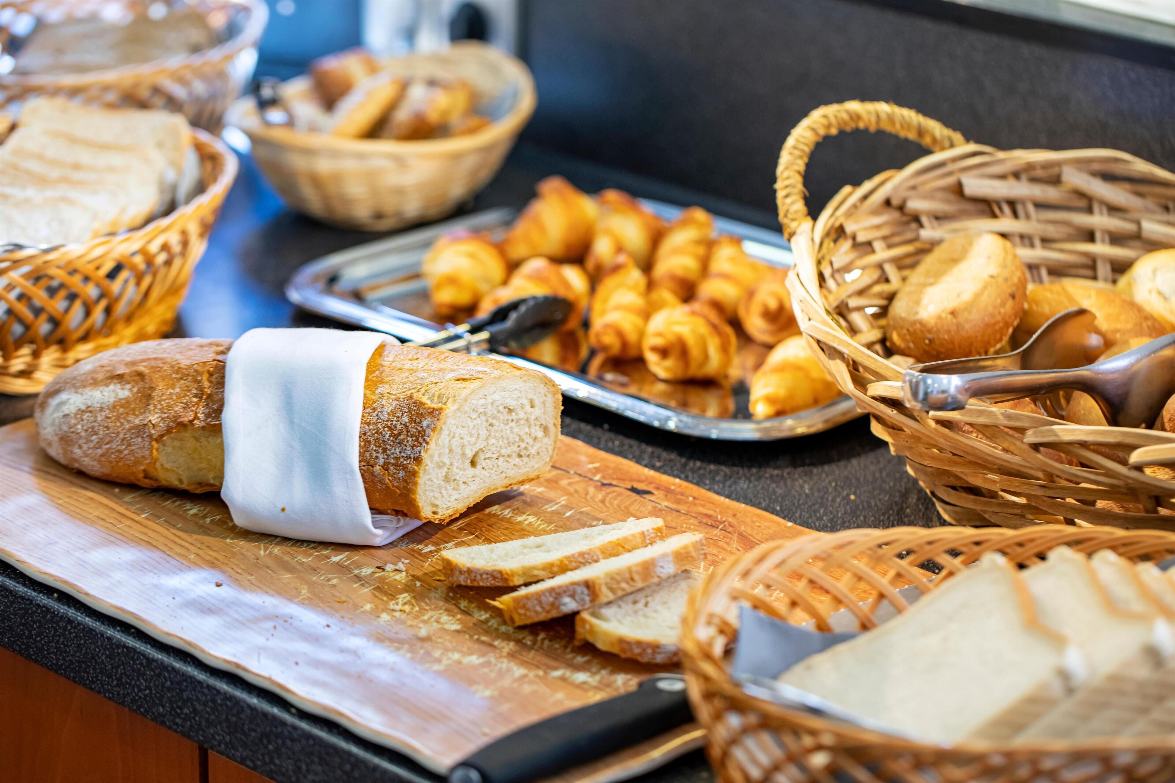 A buffet with various breads and pastries, including croissants and baguettes, arranged on a counter.