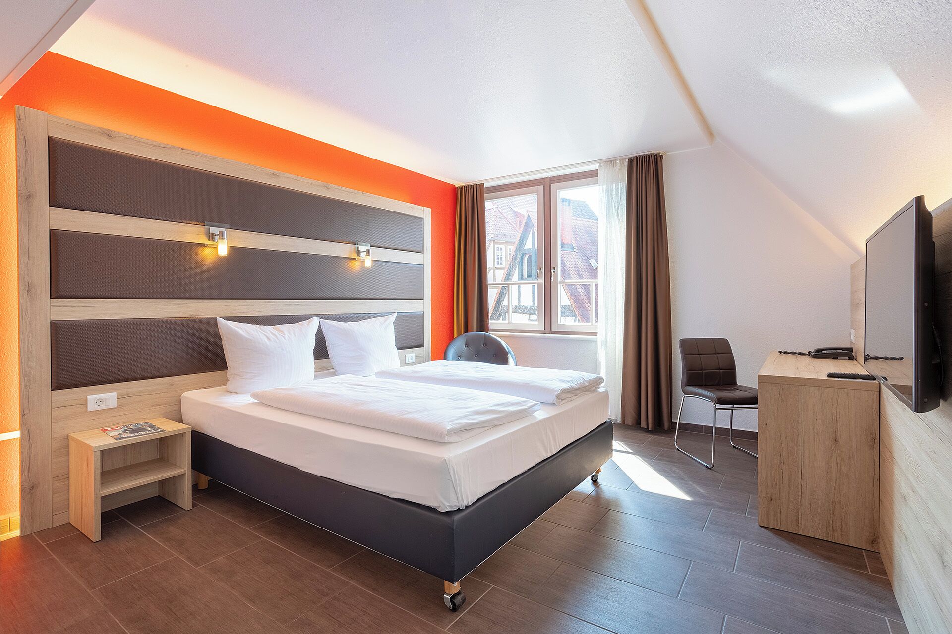 A modern hotel room with a large bed, bedside tables, a desk, and a TV.